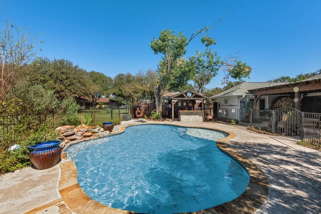 Freeform swimming pool with rock waterfall feature, stone coping, and a built-in poolside bar