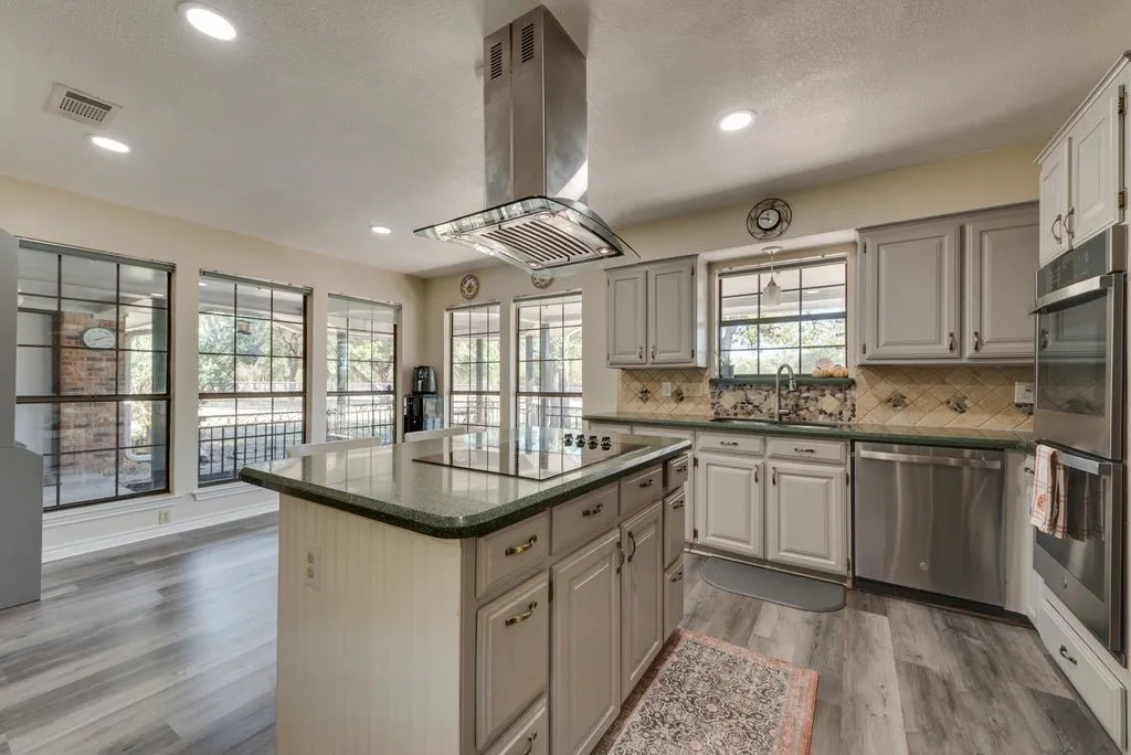 Kitchen featuring an island cooktop with a stainless steel range hood, light gray cabinetry, stainless steel appliances, and wood-finish flooring