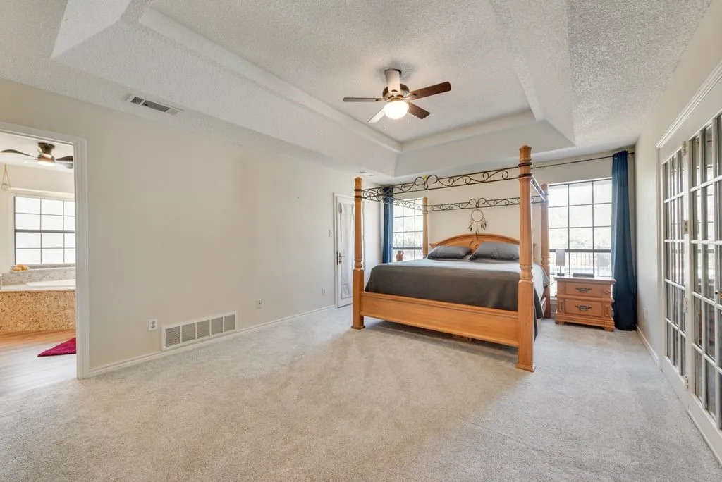 Recessed tray ceiling with a ceiling fan, light gray carpeting, and French doors with decorative glass panels