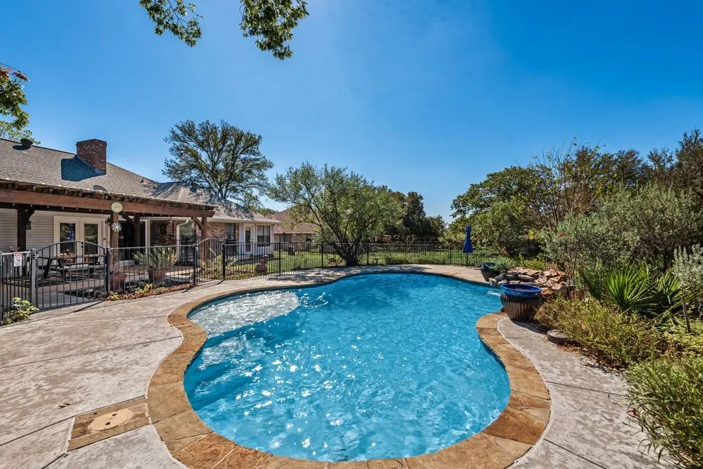Freeform swimming pool with stone coping, textured concrete decking, and a waterfall feature