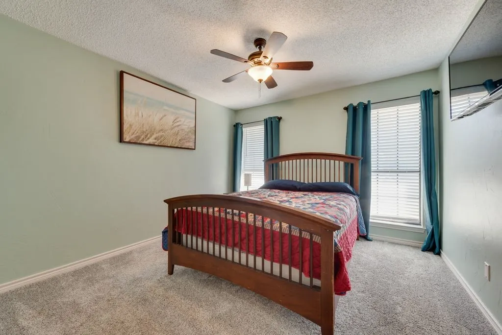 Carpeted flooring, two windows with blinds and curtains, ceiling fan with integrated lighting, light-colored walls