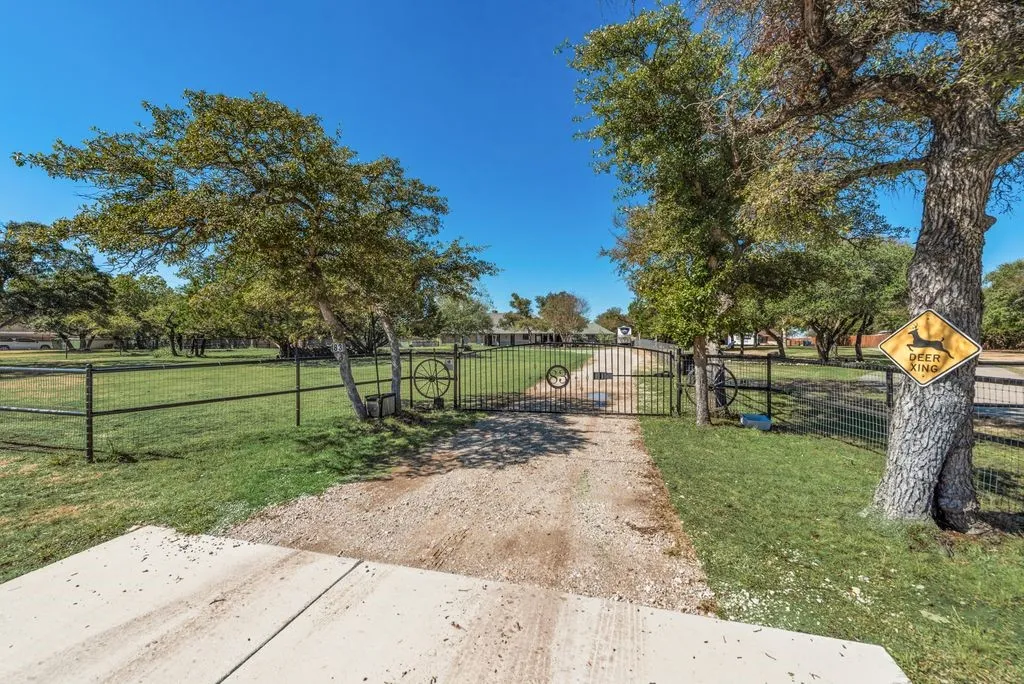 Gated entry with a gravel driveway, surrounded by mature trees, and a wire mesh fence