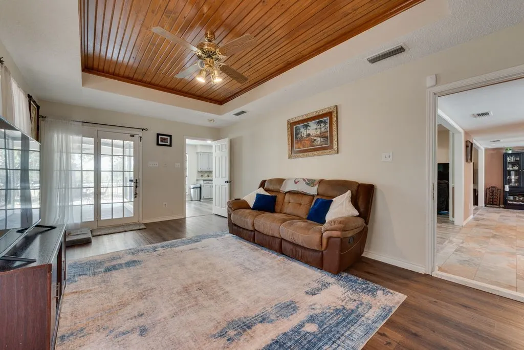 Wood-finish flooring, recessed wood-paneled ceiling with a brass-finish ceiling fan, and French doors