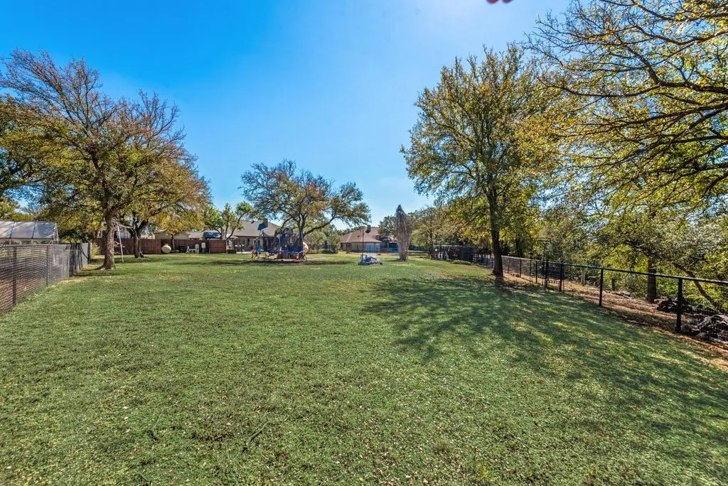 Expansive lawn featuring mature trees and perimeter fencing