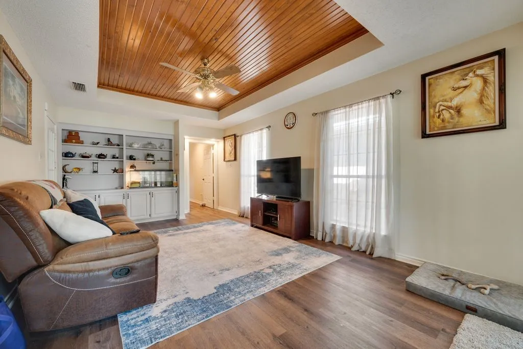 Wood-finish flooring throughout, tray ceiling with wood paneling, recessed lighting, and a built-in shelving unit with lower cabinetry