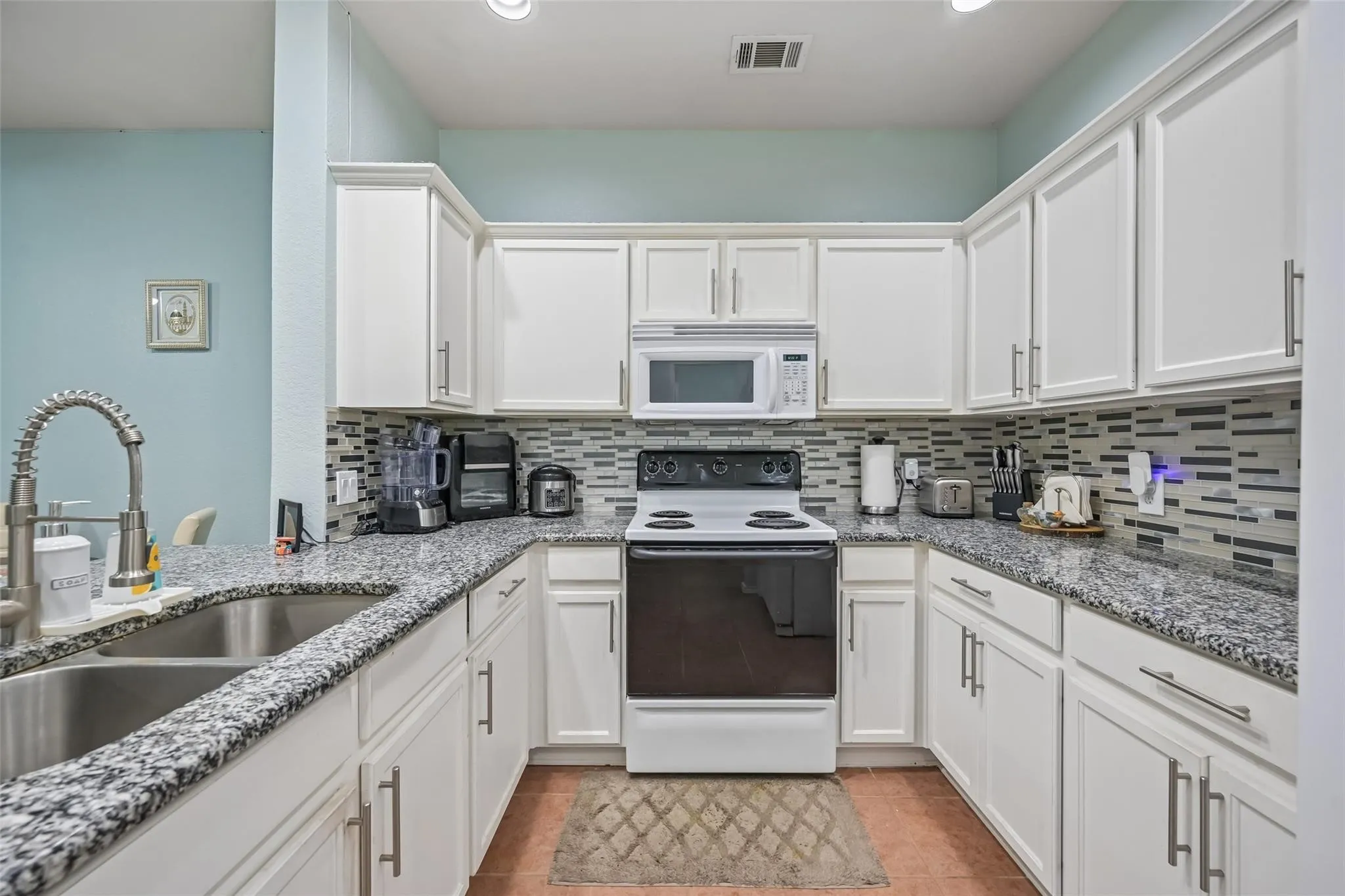 U-shaped kitchen featuring white cabinetry, speckled countertops, a double basin sink with gooseneck faucet, a white range, and a patterned tile backsplash