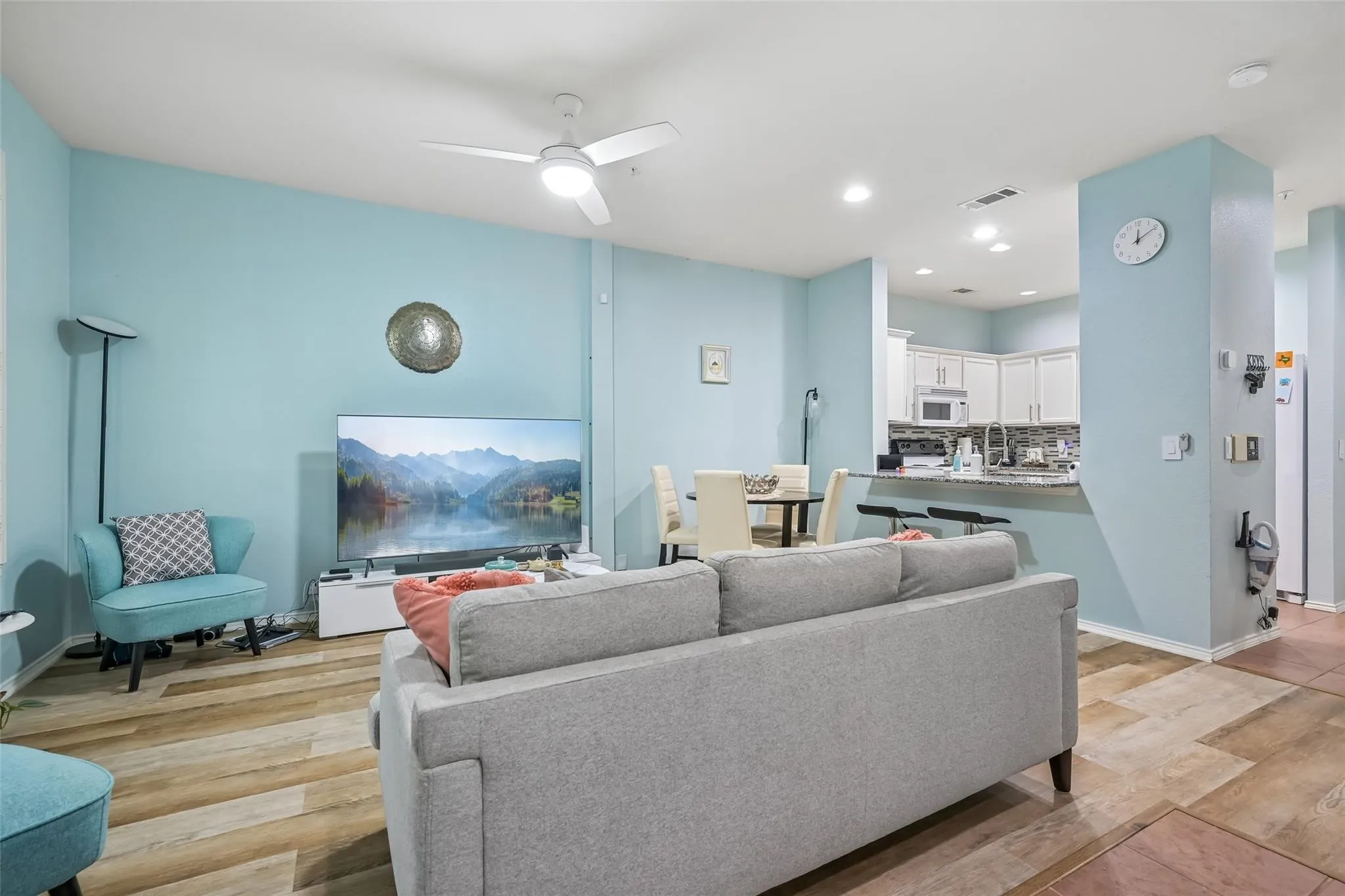 Open-concept living space featuring wood-finish flooring, a ceiling fan with integrated lighting, recessed lighting, and a kitchen with white cabinetry