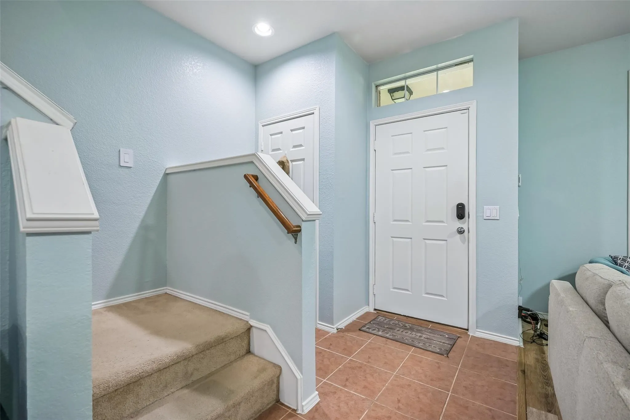 Entryway featuring a paneled door, transom window, recessed lighting, tile flooring, and a carpeted staircase with a wood-finish handrail