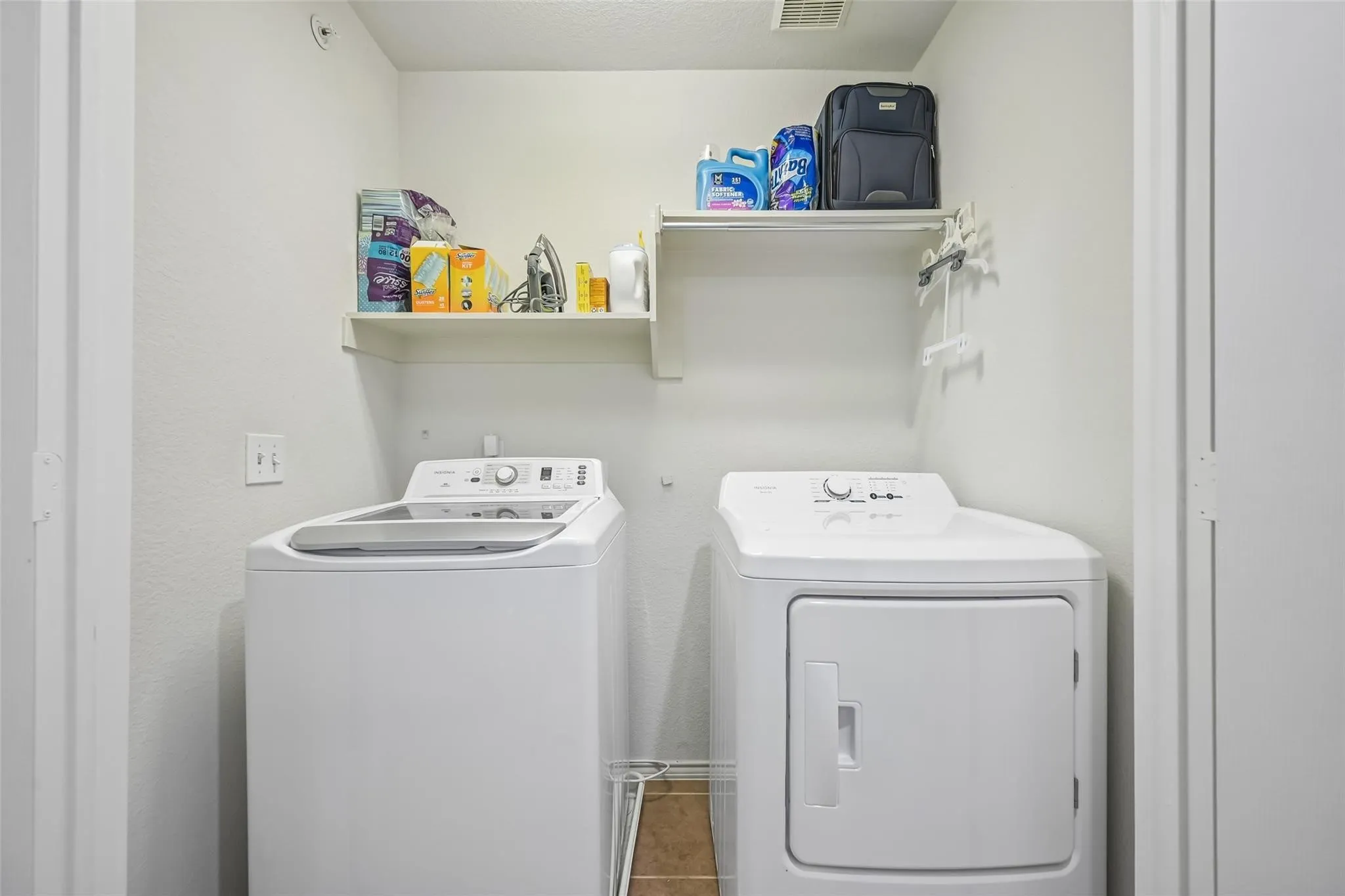 Dedicated laundry area featuring a washer and dryer, wall-mounted shelving, and tile flooring