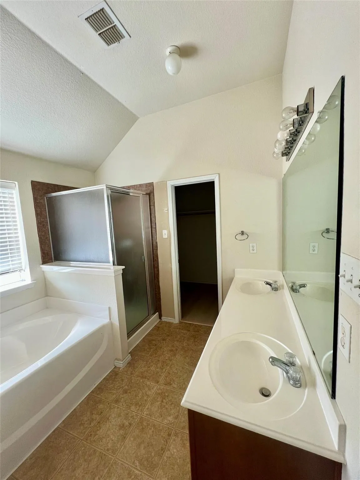 Bathroom featuring dual vanity with integrated sinks, built-in bathtub, glass-enclosed shower, and tile flooring