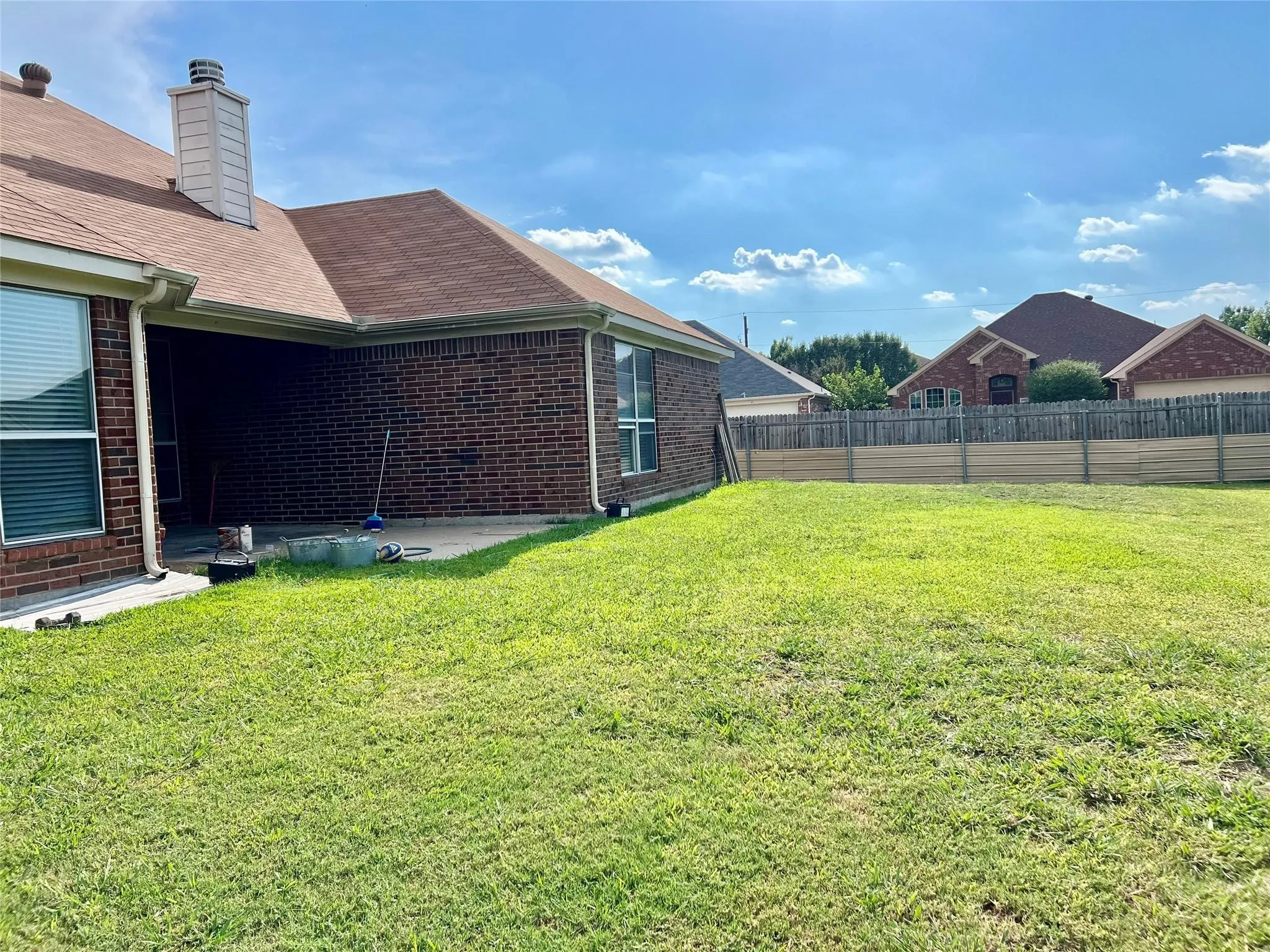 Expansive backyard featuring a manicured lawn, brick exterior, covered patio, and privacy fencing