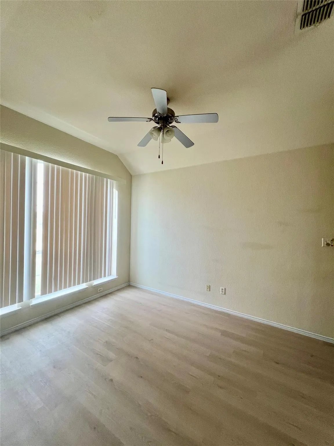 Wood-finish flooring, vaulted ceiling, ceiling fan with integrated lighting, window with vertical blinds
