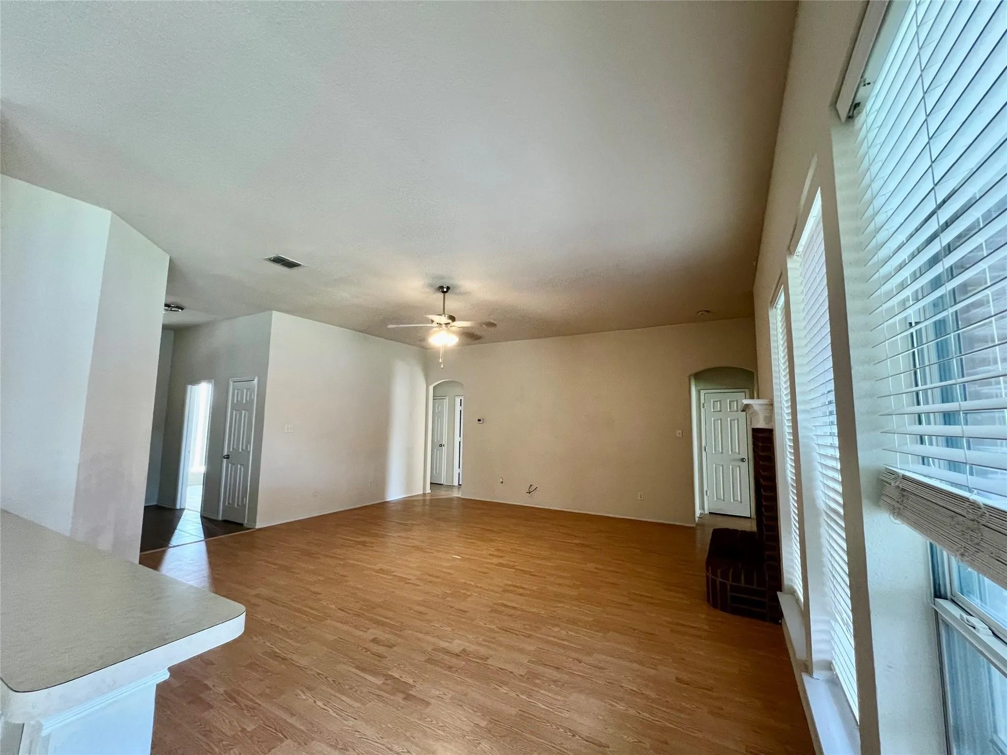 Wood-finish flooring throughout, ceiling fan with integrated lighting, window blinds, and arched doorways