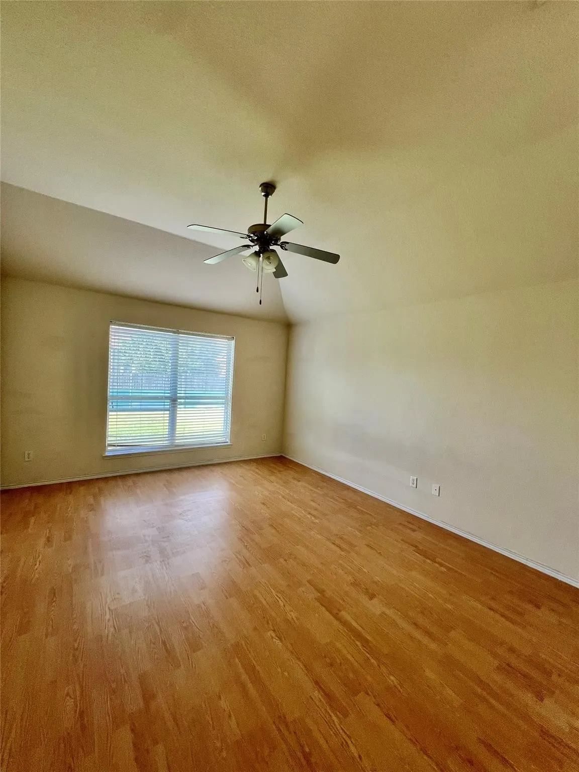 Vaulted ceiling with a ceiling fan, wood-finish flooring, and a large window with blinds