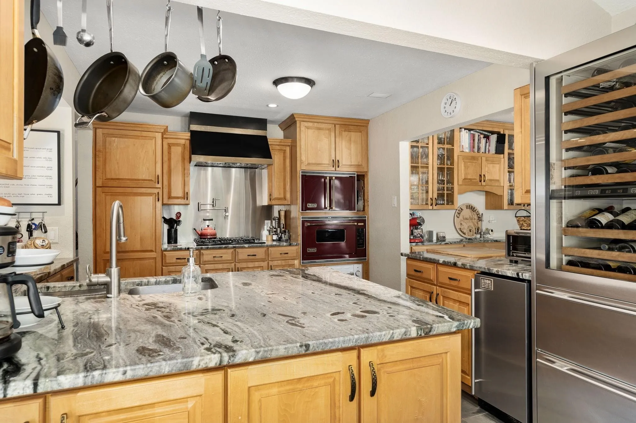 Kitchen featuring wood cabinetry, a large kitchen island with a built-in sink, stainless steel appliances, and a built-in wine refrigerator