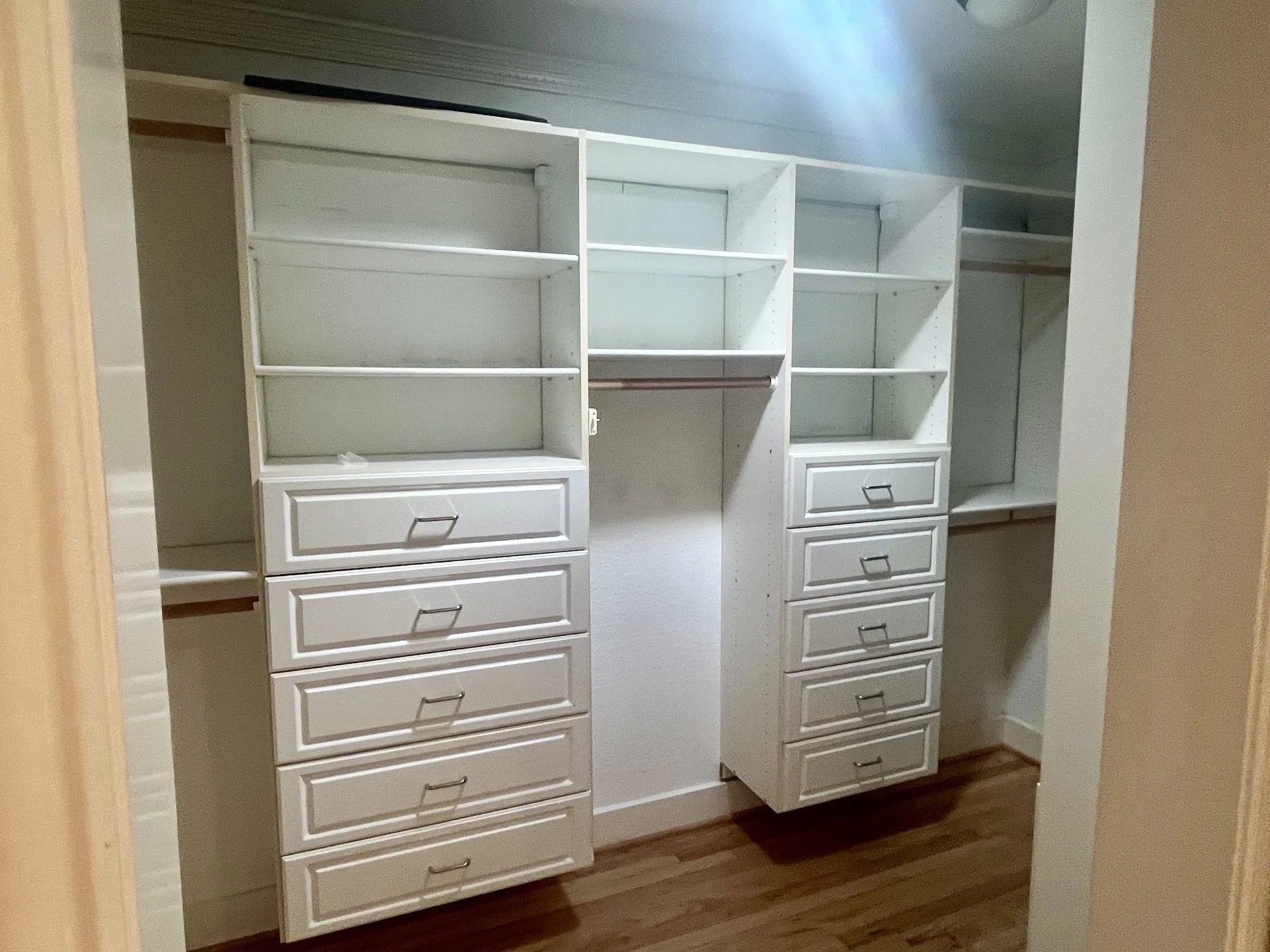 Custom walk-in closet featuring built-in white cabinetry with multiple shelving units, five spacious drawers with metal hardware, and a central hanging rod for optimal storage and organization