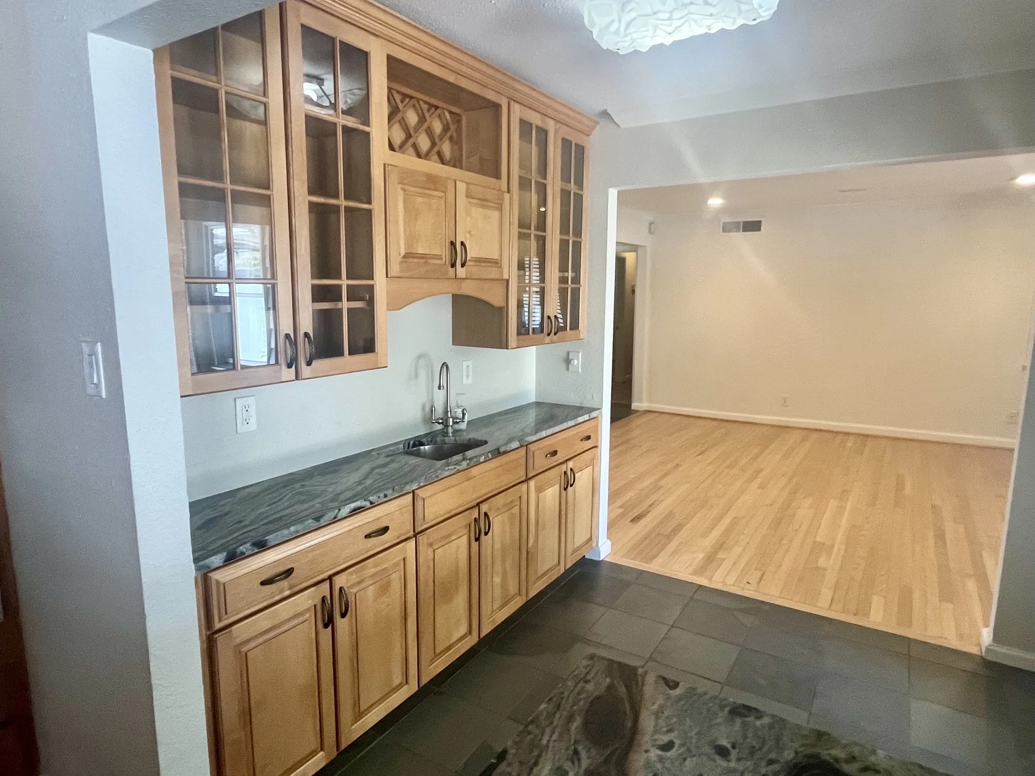 Wet bar featuring wood cabinetry with glass-front uppers, a built-in wine rack, and a dark stone countertop with an undermount sink