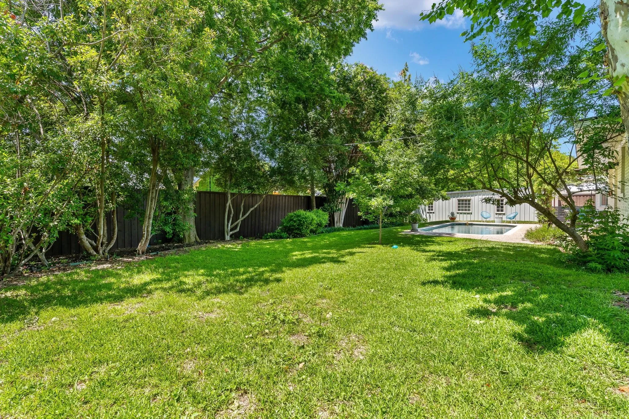 Expansive green lawn, mature trees, privacy fencing, and a built-in swimming pool with surrounding hardscaping
