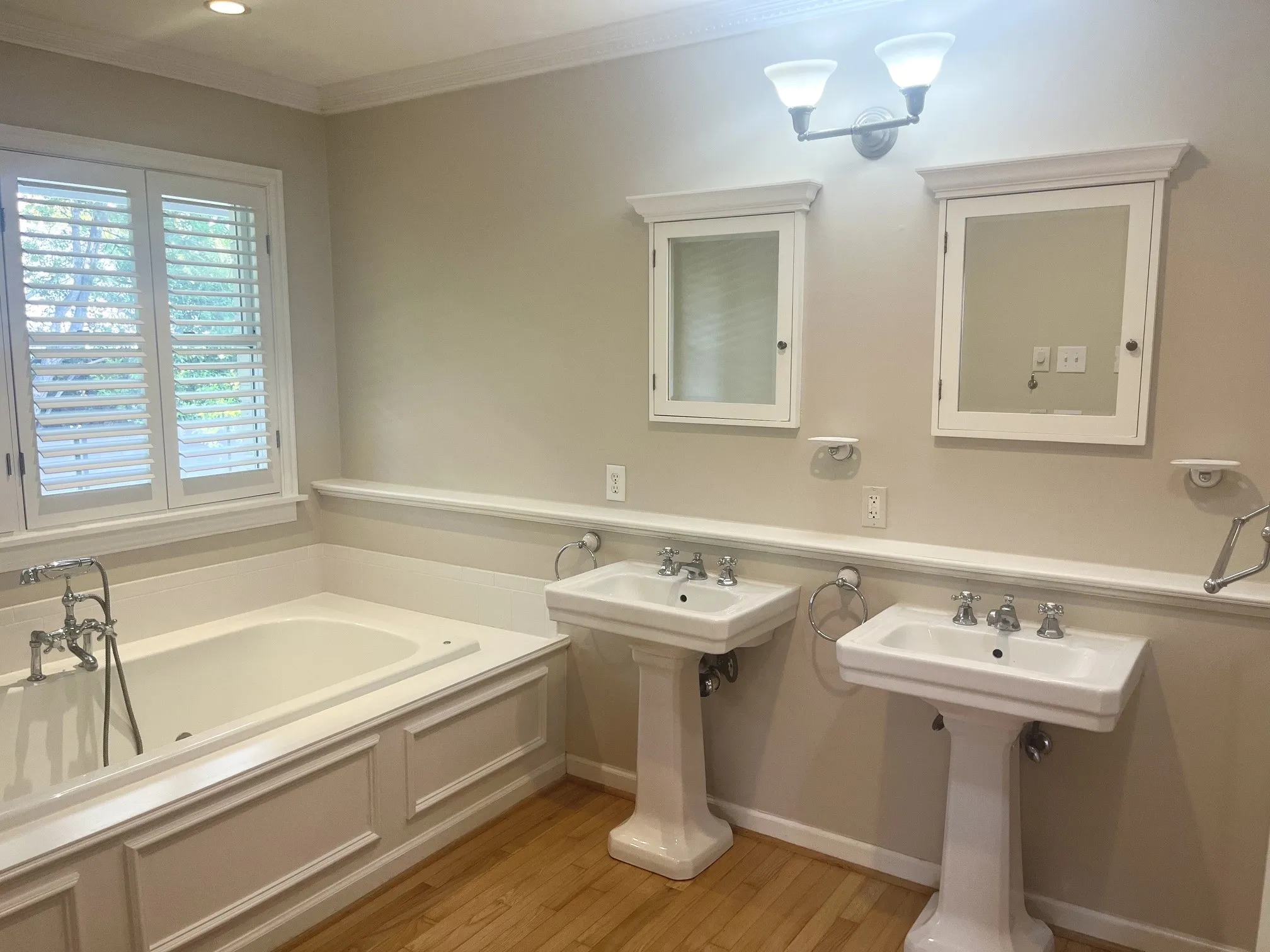 Built-in soaking tub with panel detailing, dual pedestal sinks, and two recessed medicine cabinets
