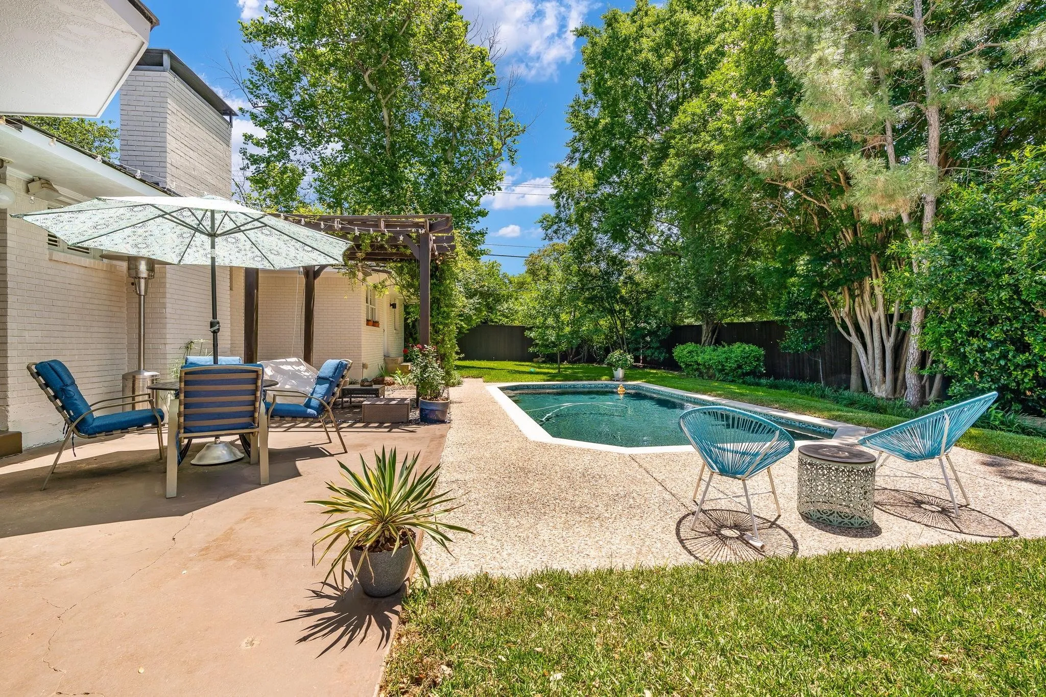 Backyard with a swimming pool, concrete patio, and mature trees