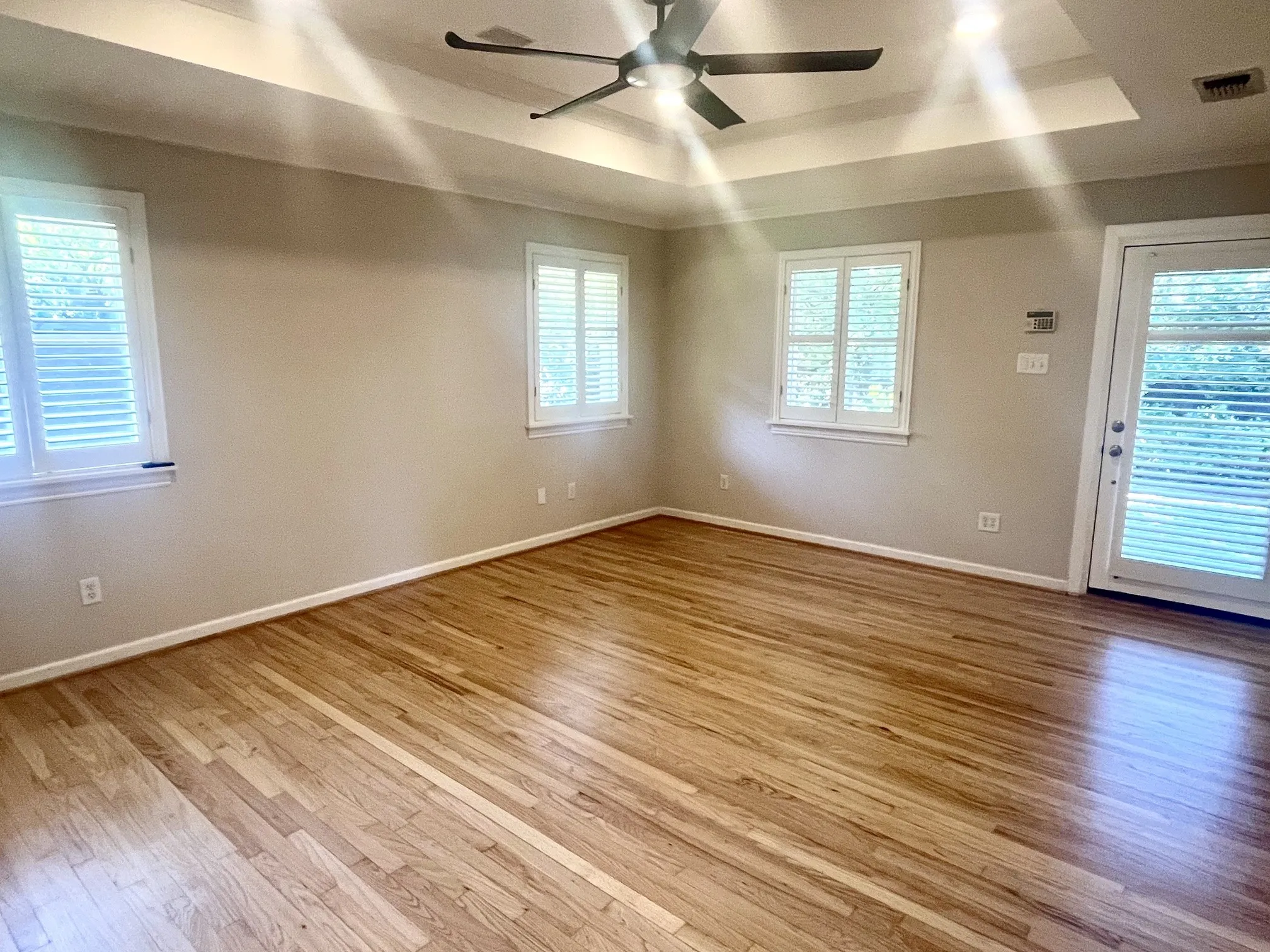 Hardwood flooring throughout, tray ceiling, ceiling fan, white window shutters, and a glass-paneled door