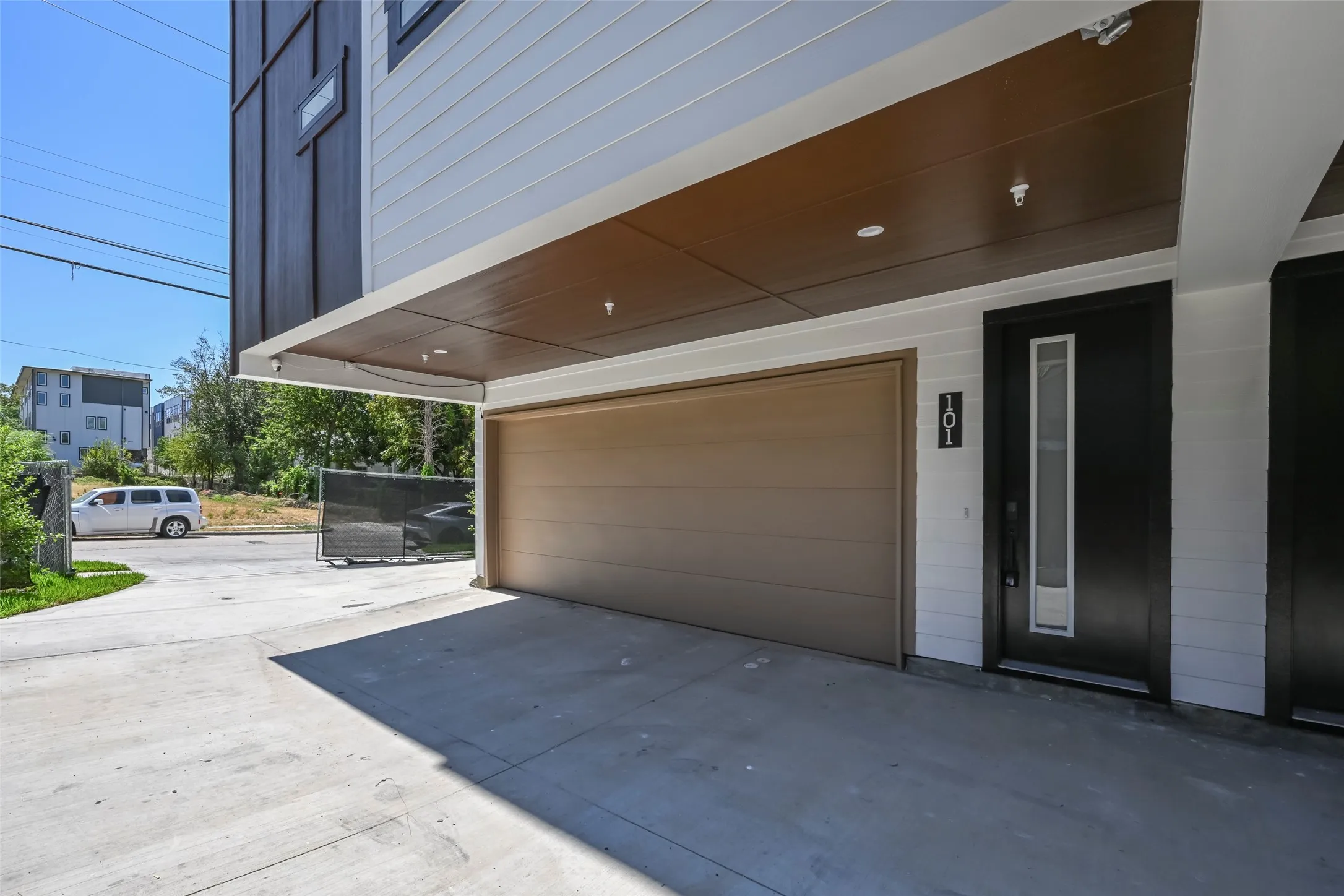Concrete driveway with a covered entry, featuring a brown garage door, dark entry door with vertical window, and light gray siding