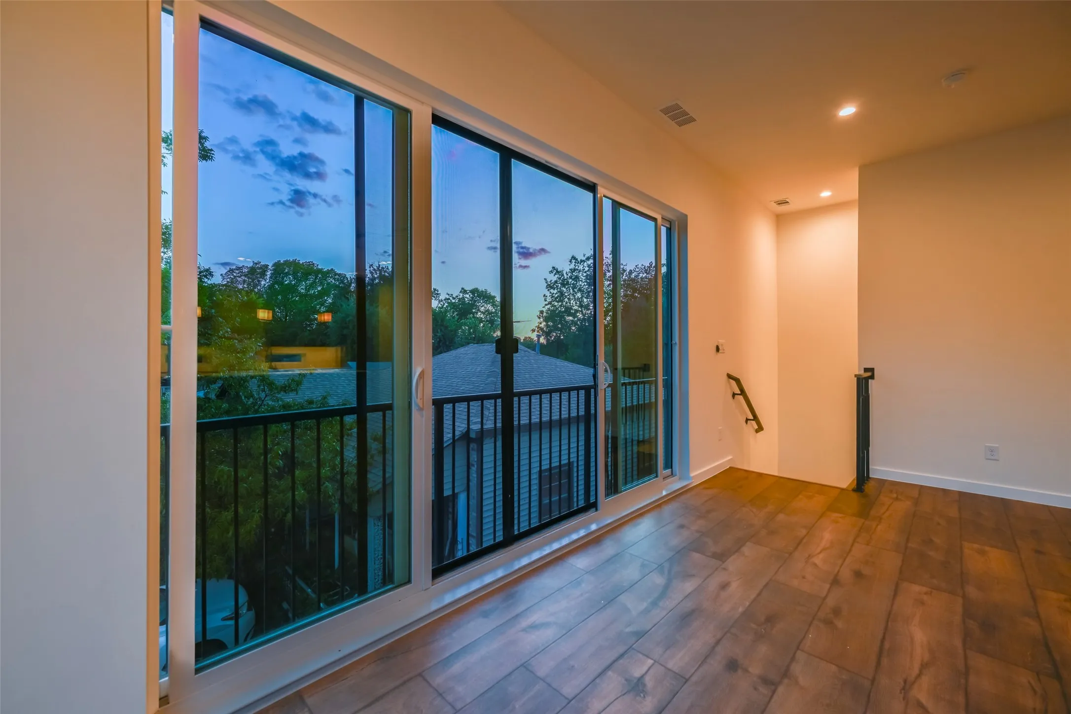 Wood-finish flooring with a large sliding glass door opening to a private balcony with black metal railing