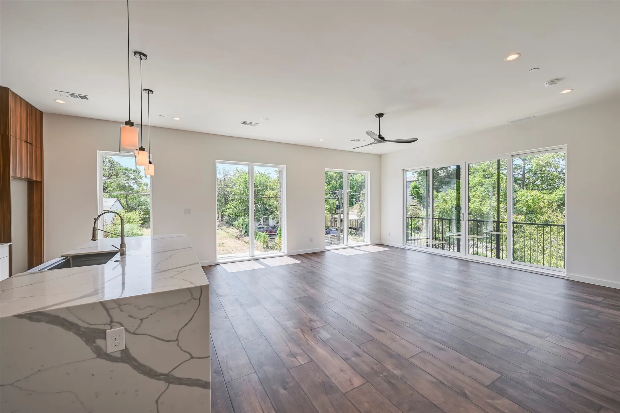 Open-concept living space featuring wood-finish flooring, recessed lighting, a ceiling fan, and large sliding glass doors leading to balconies