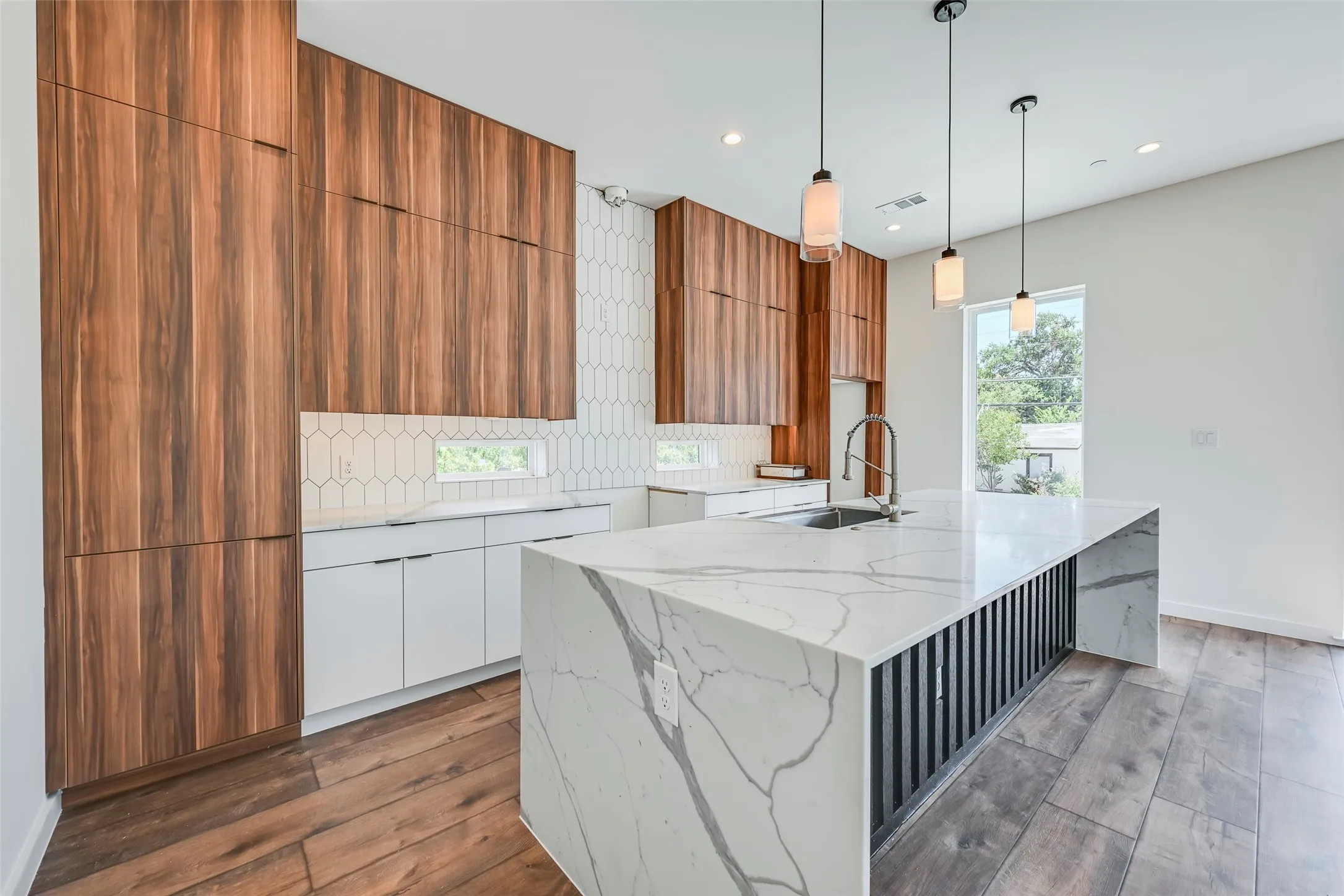 Kitchen featuring a substantial island with a waterfall counter, wood-finish flooring, full-height wood cabinetry, white shaker-style lower cabinetry, and a geometric tile backsplash