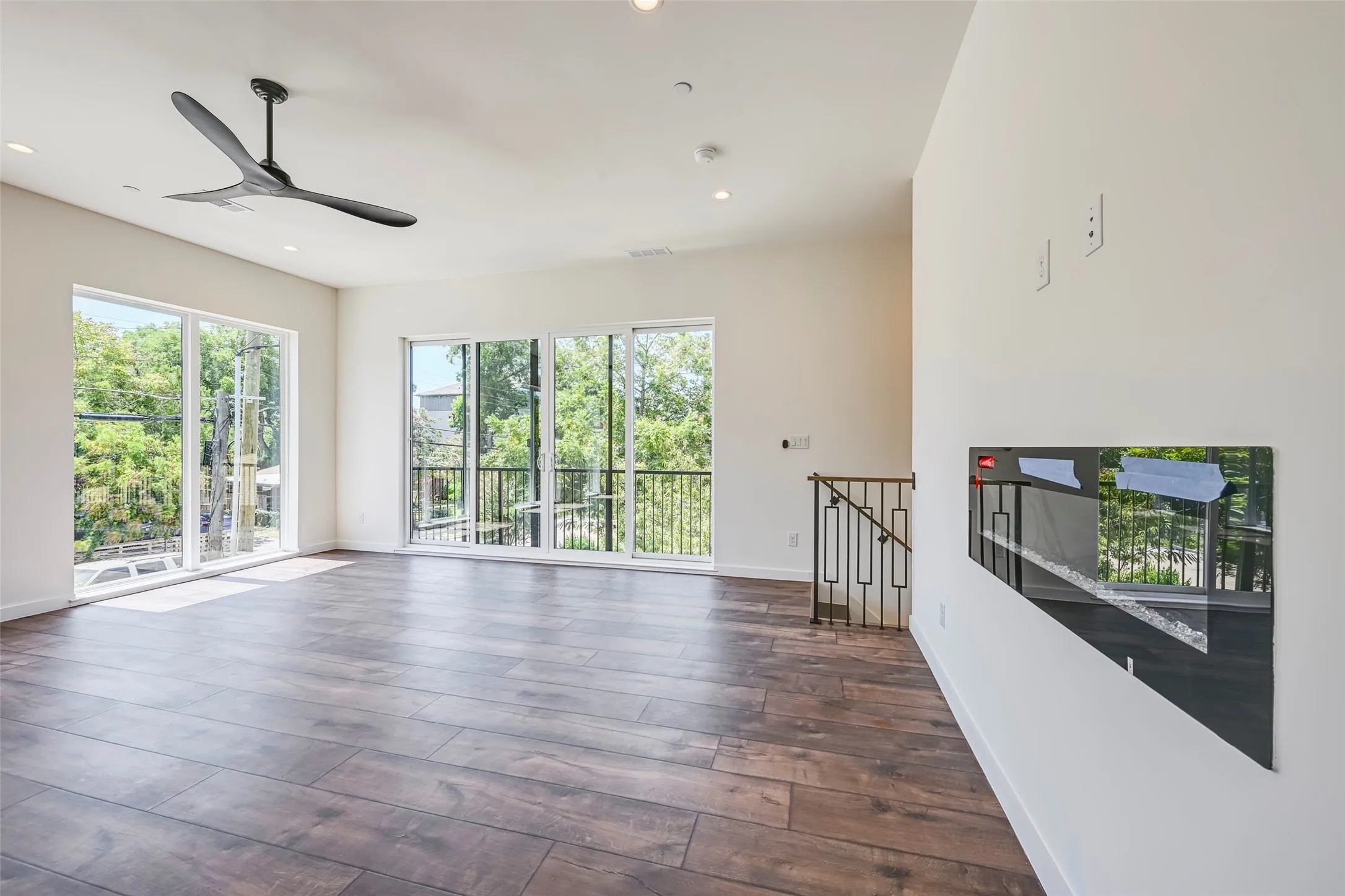 Wood-finish flooring, recessed lighting, ceiling fan, multiple glass doors, and a decorative railing