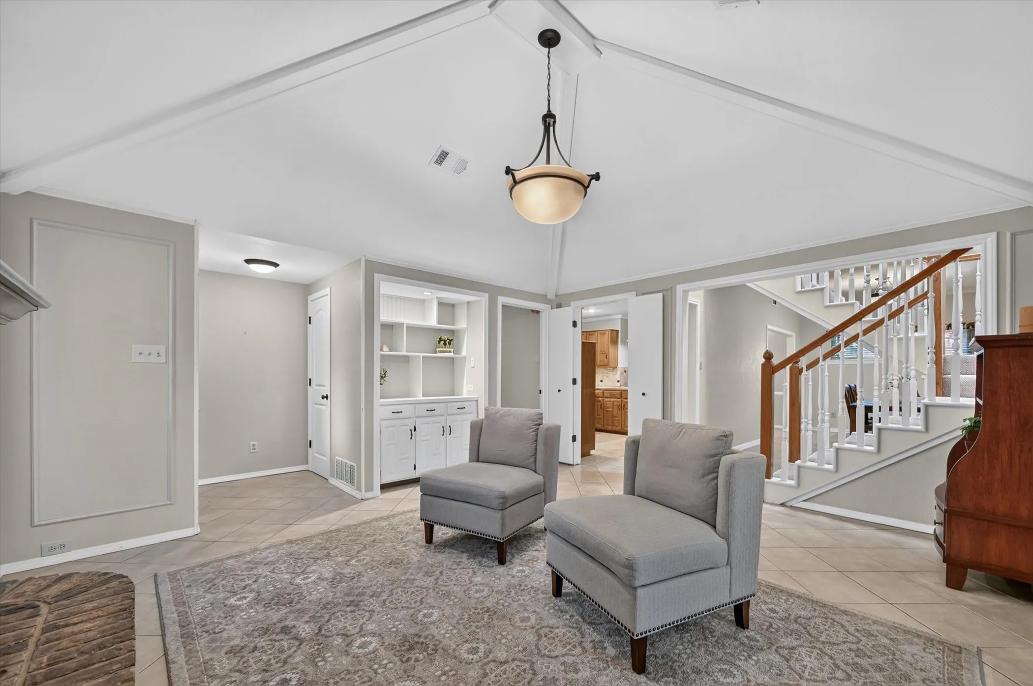 The living room has a vaulted ceiling, tile floors , lighted custom built in display cabinet and looks into the kitchen and dining area.