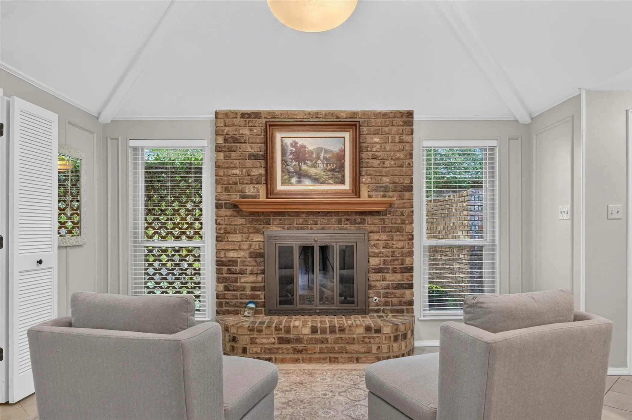 Downstairs living room has a brick gas start fireplace that is framed by windows that allow for natural light.