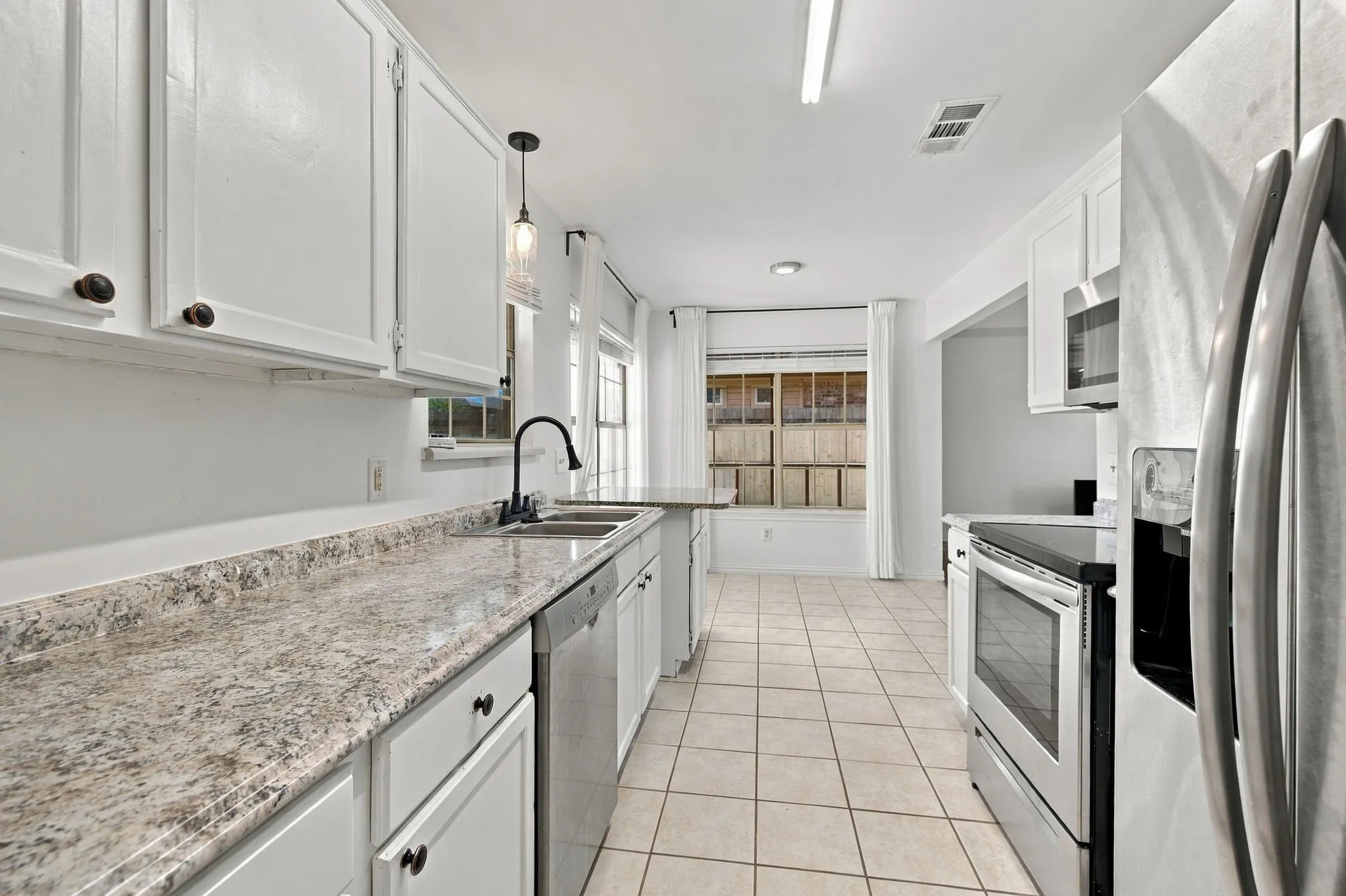 White cabinetry, speckled countertops, stainless steel appliances, tile flooring, and a double basin sink with a gooseneck faucet