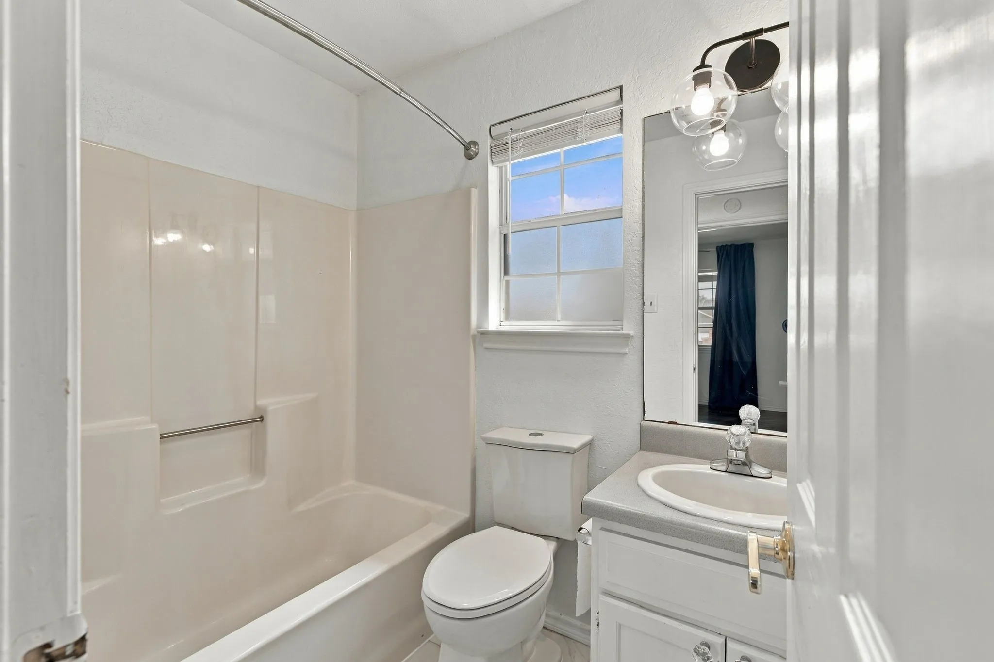 White vanity with integrated sink, rectangular mirror, and a three-bulb sconce