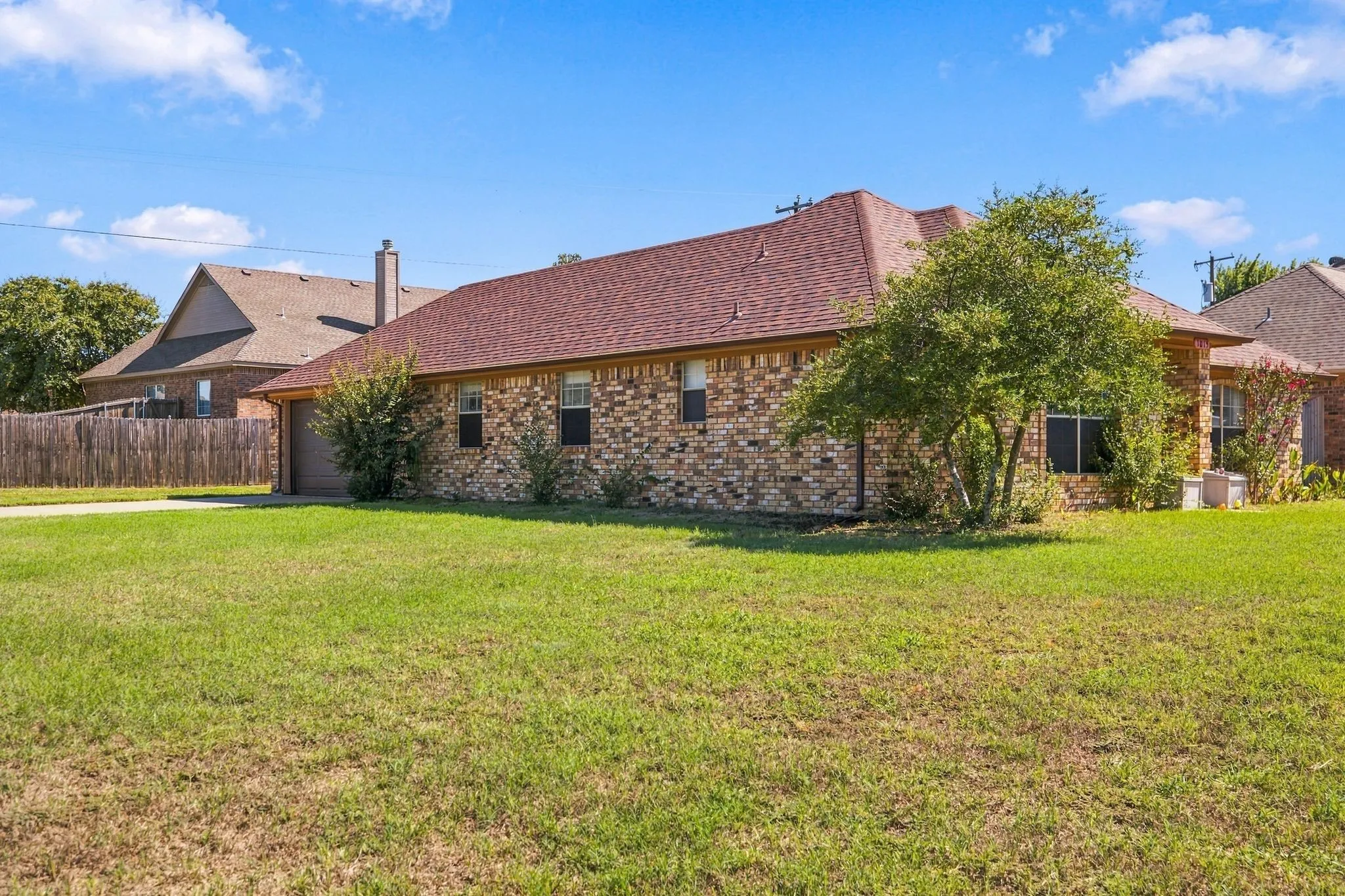 Brick exterior, red shingle roof, attached garage, established landscaping, and a manicured lawn
