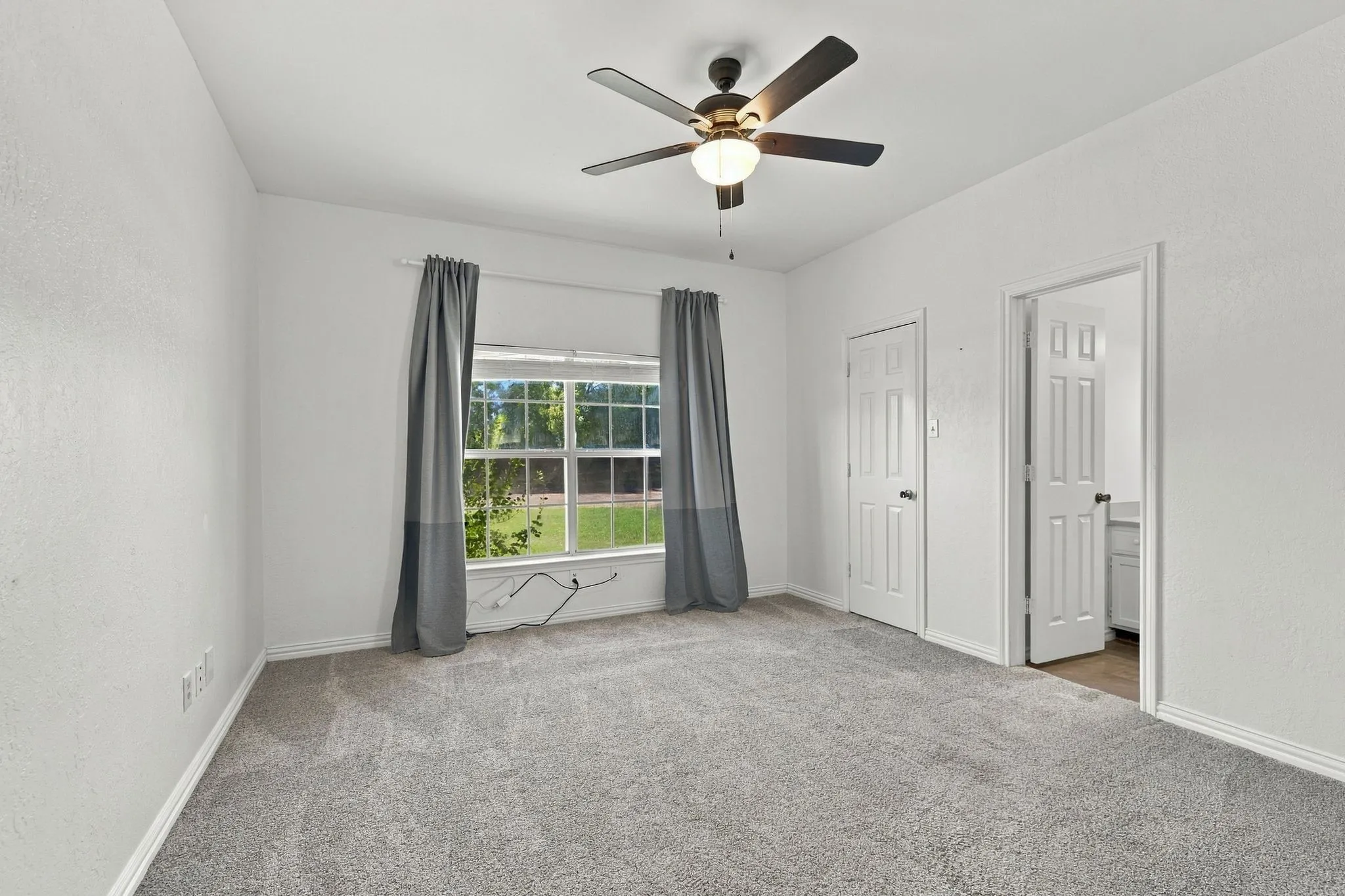 Expansive room with neutral carpeting, a ceiling fan with integrated lighting, and a large window