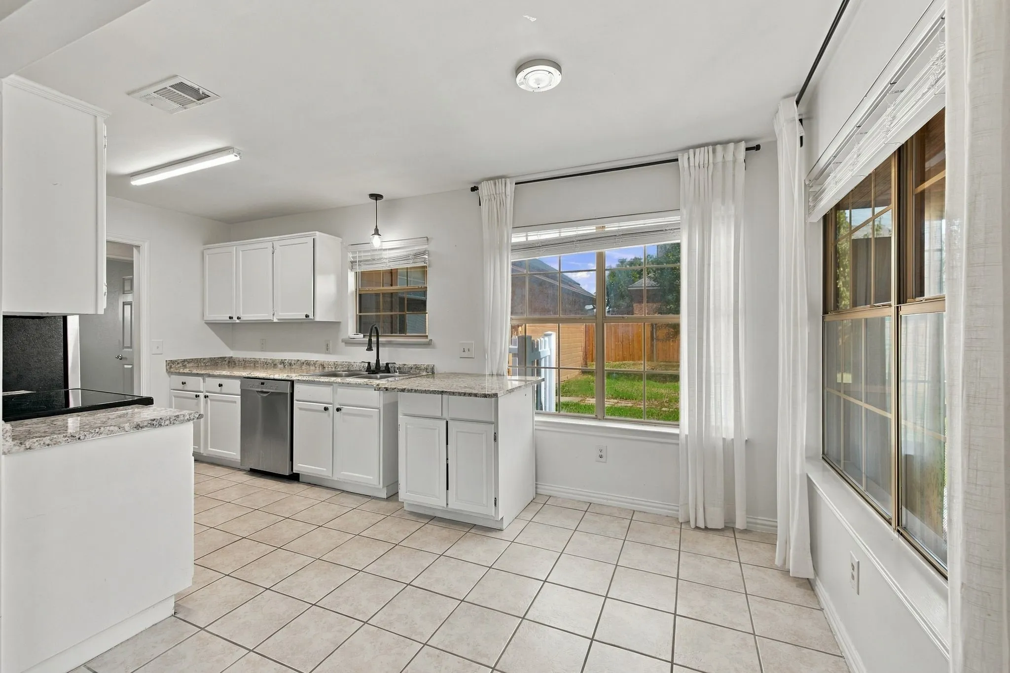 Kitchen featuring white cabinetry, light-toned countertops, a stainless steel dishwasher, a black cooktop, and tile flooring