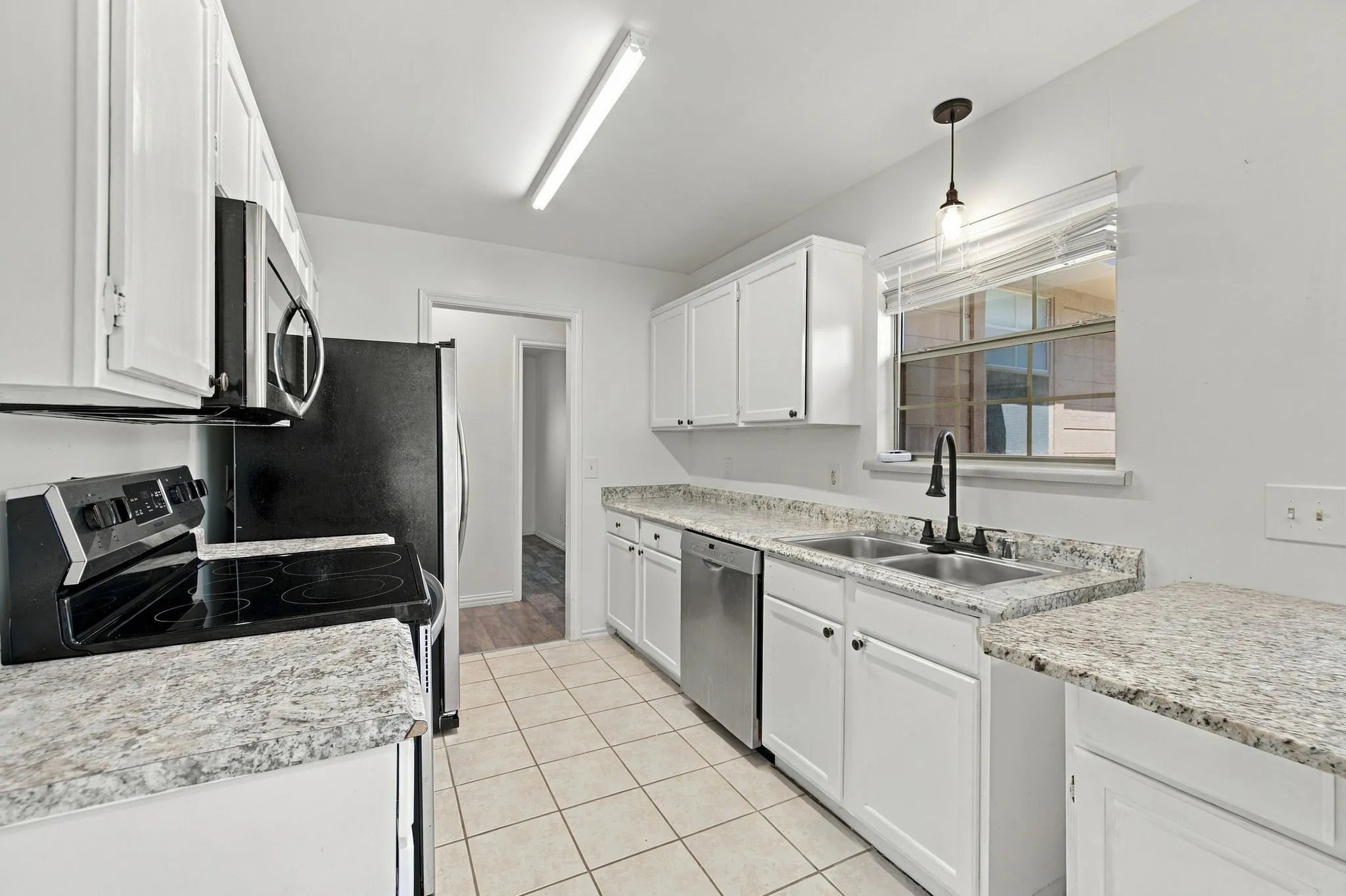 Kitchen featuring white cabinetry, granite-look countertops, stainless steel sink, black range, and tile flooring