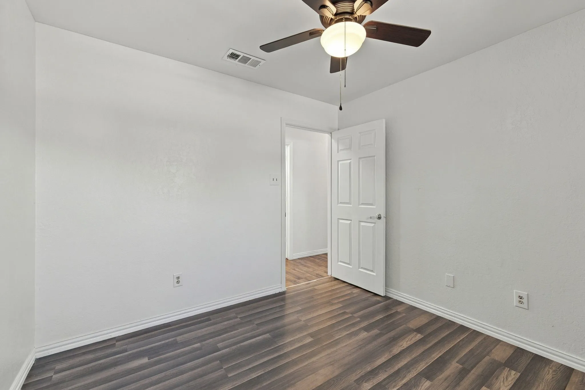 Wood-finish flooring, white paneled door, and a ceiling fan with integrated lighting