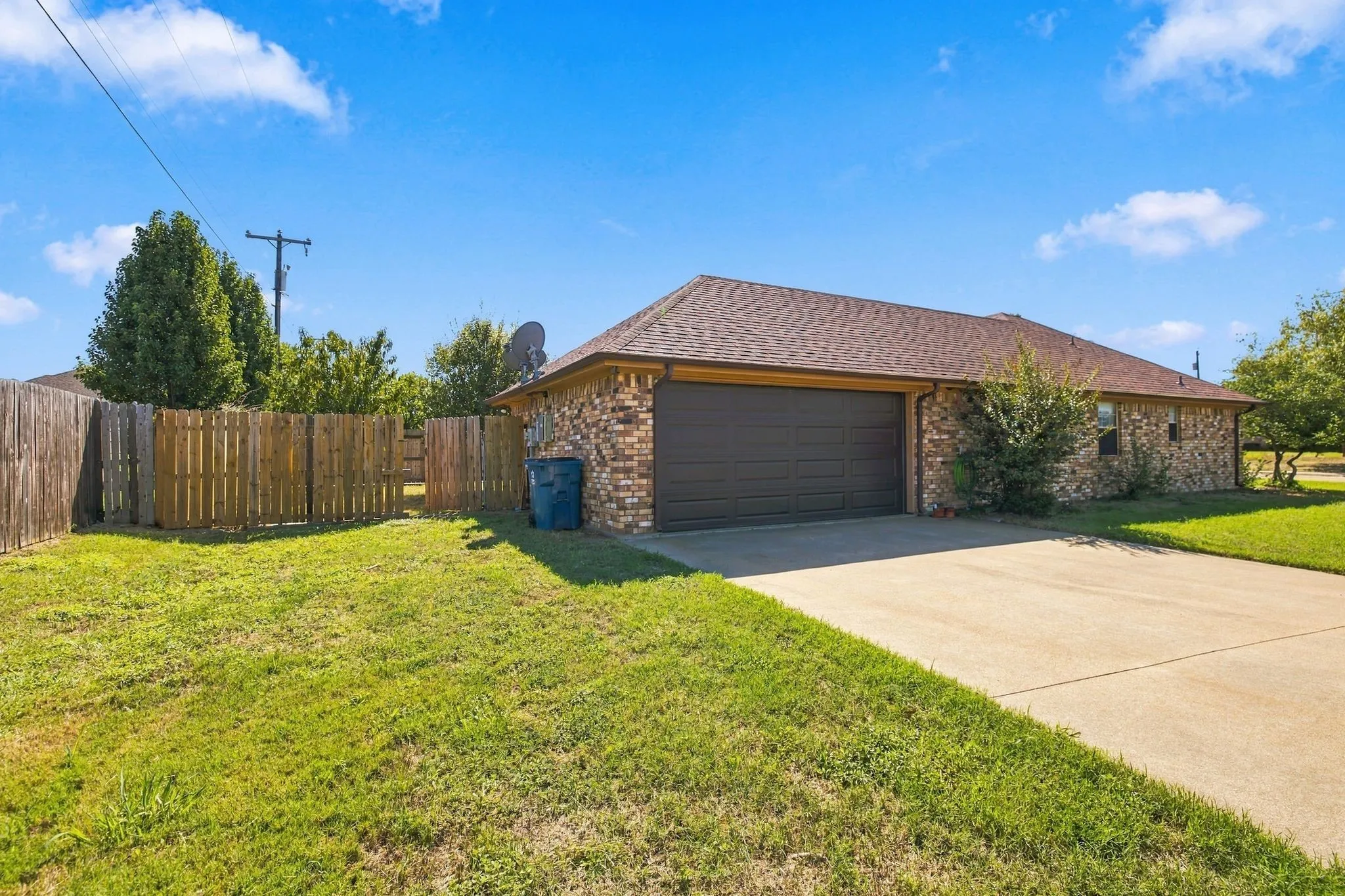 Brick exterior with an attached garage, paved driveway, and a fenced backyard