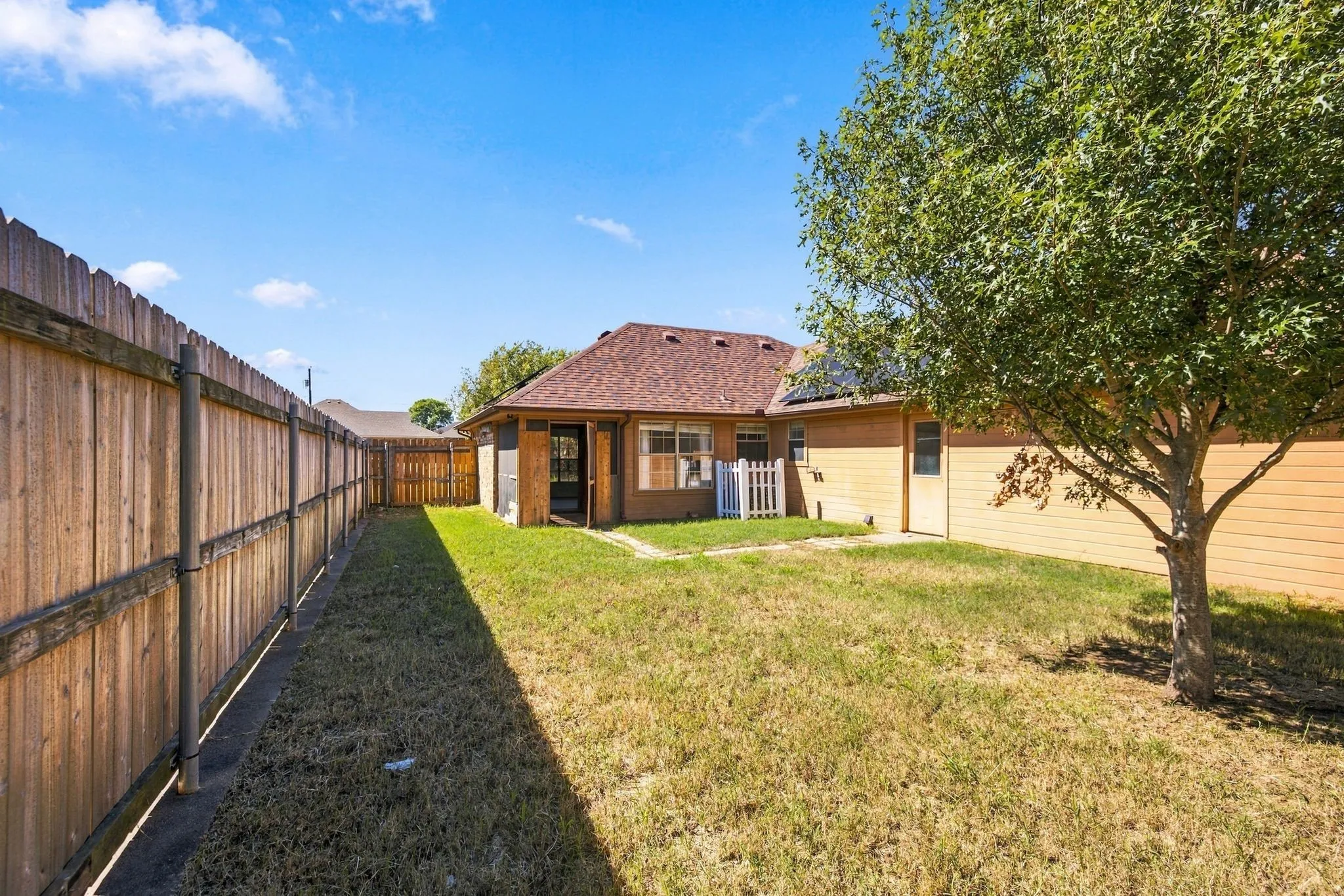Private backyard featuring a full wood fence, mature tree, and a secondary side door