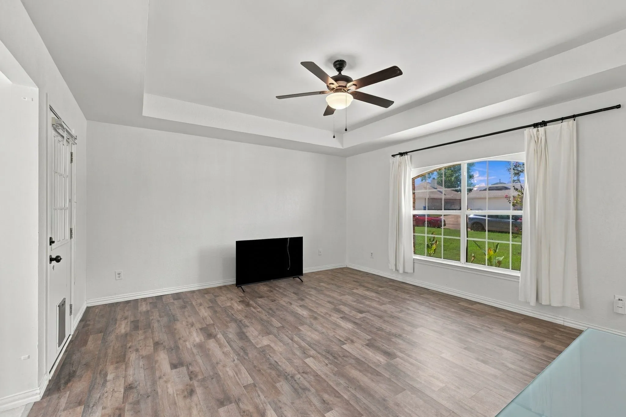 Spacious room featuring wood-finish flooring, a tray ceiling, and a ceiling fan with light fixture