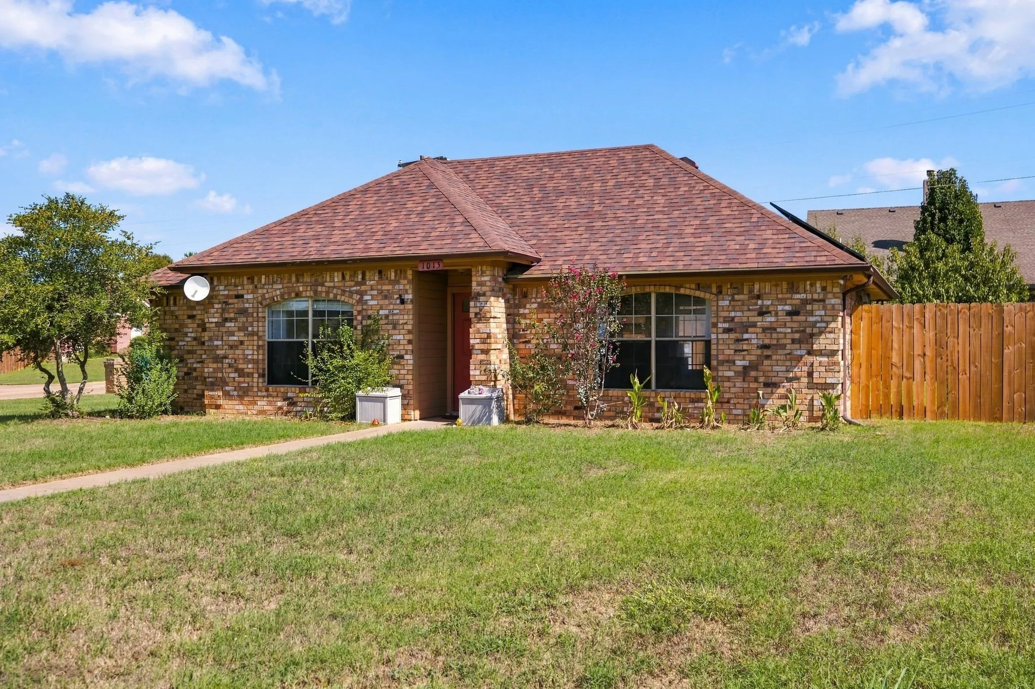 Brick facade residence featuring a shingle roof, arched windows, and a wood privacy fence