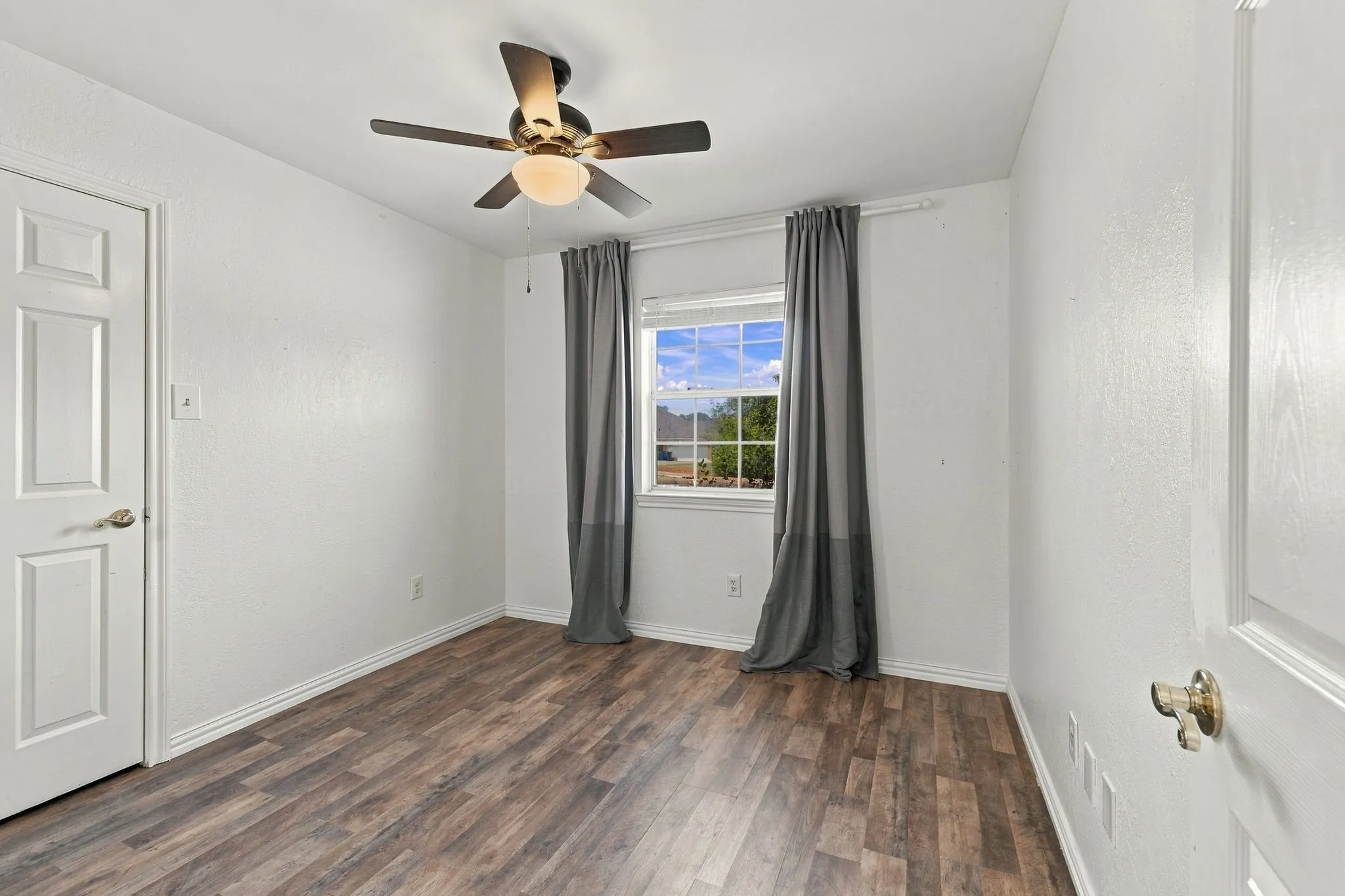 Recessed window with gray drapes, wood-finish flooring, and a ceiling fan with integrated lighting