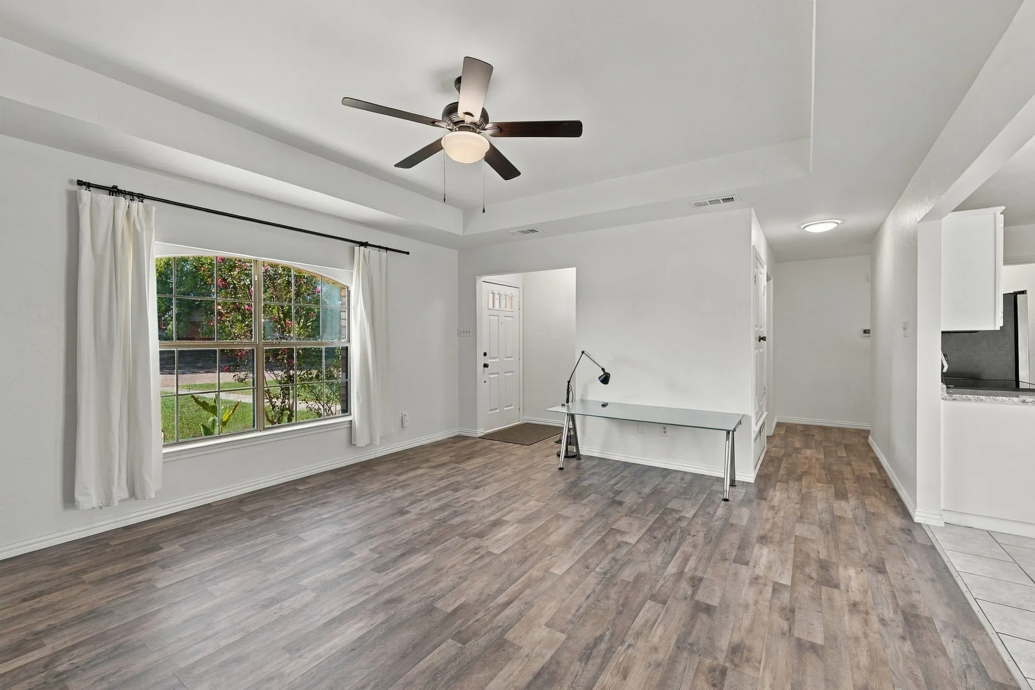 Tray ceiling with a ceiling fan light fixture, wood-finish flooring, a large arched window, and a paneled entry door