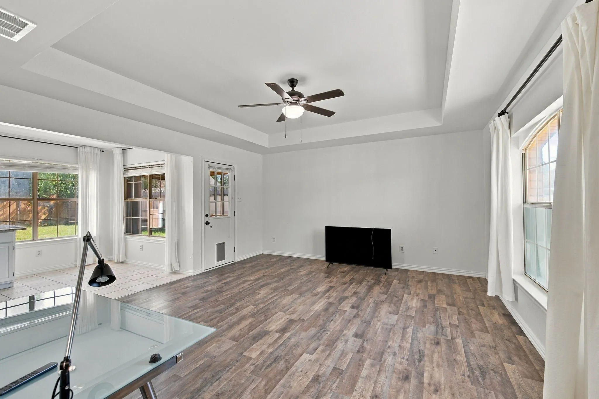 Tray ceiling with recessed lighting, wood-finish flooring, ceiling fan, and multiple windows