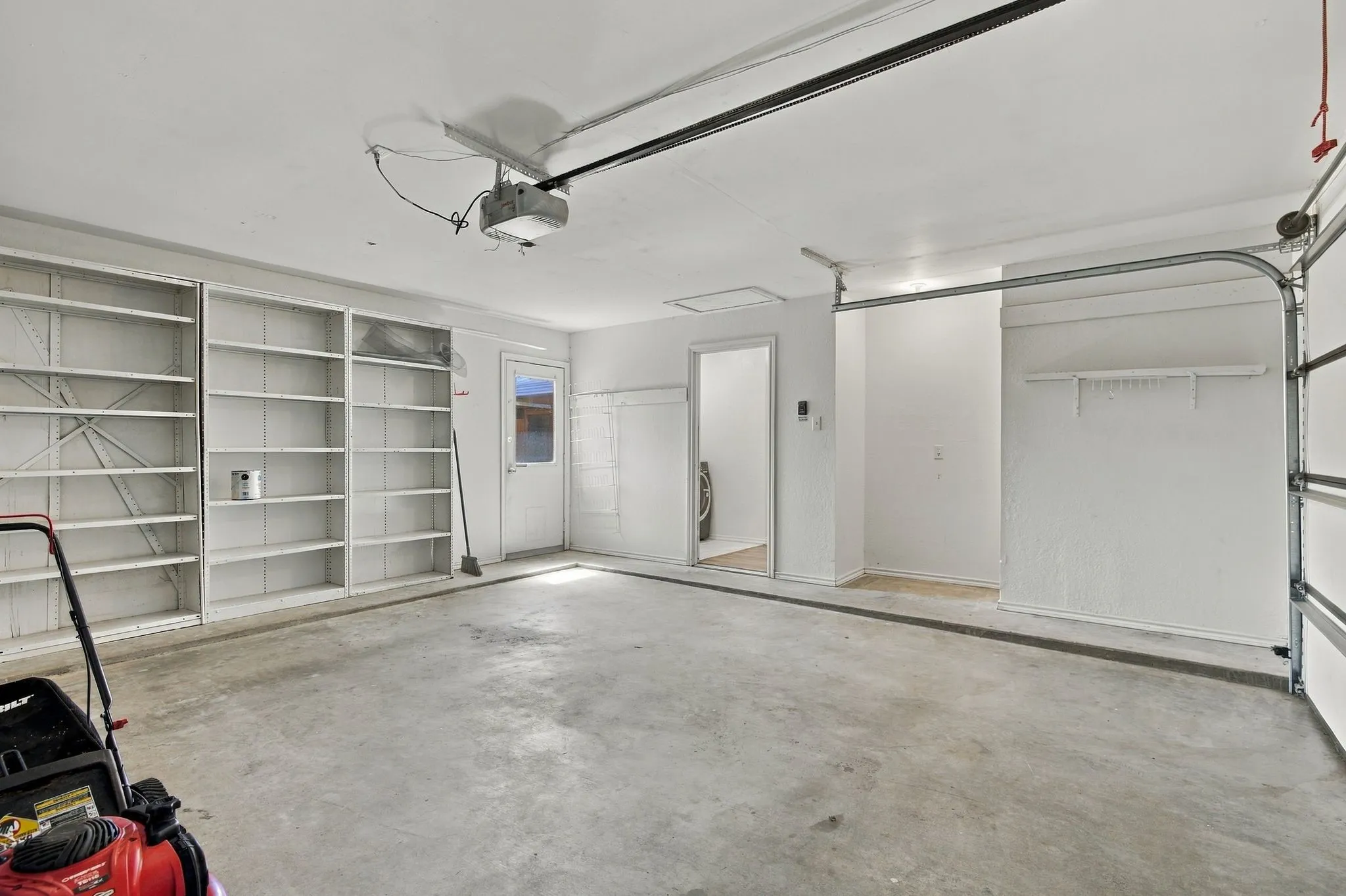 Concrete flooring, extensive built-in shelving, overhead garage door opener, interior access door, additional storage alcove
