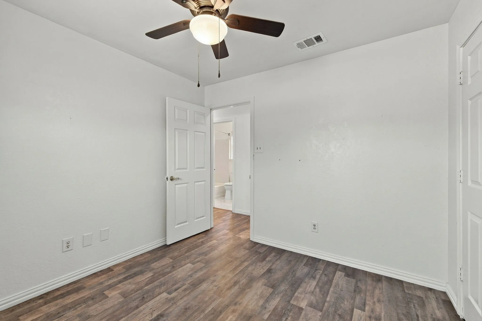 Wood-finish flooring, white walls, and a ceiling fan with integrated lighting