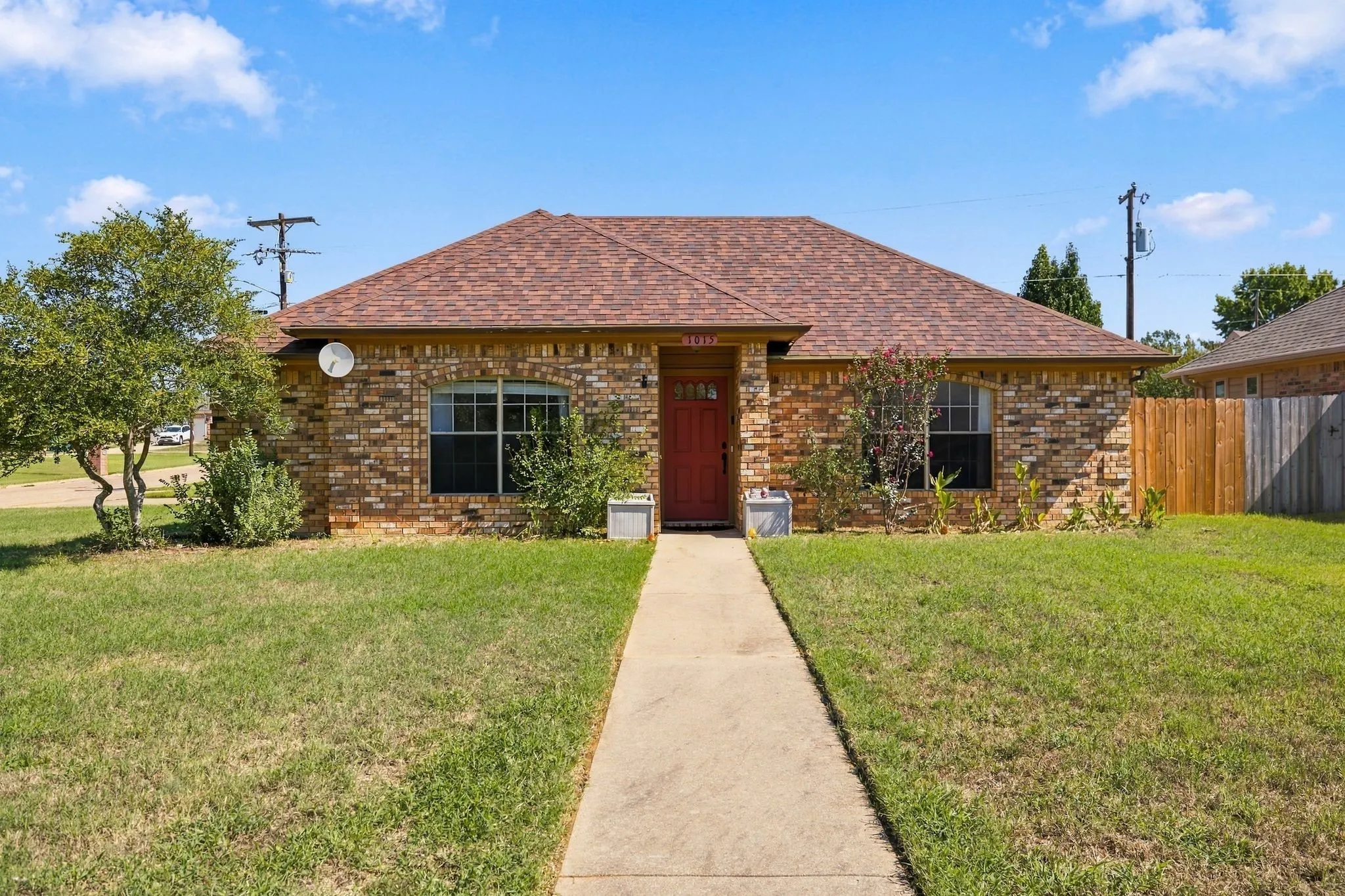 Brick exterior residence featuring a red entry door, gabled roof, and a concrete pathway