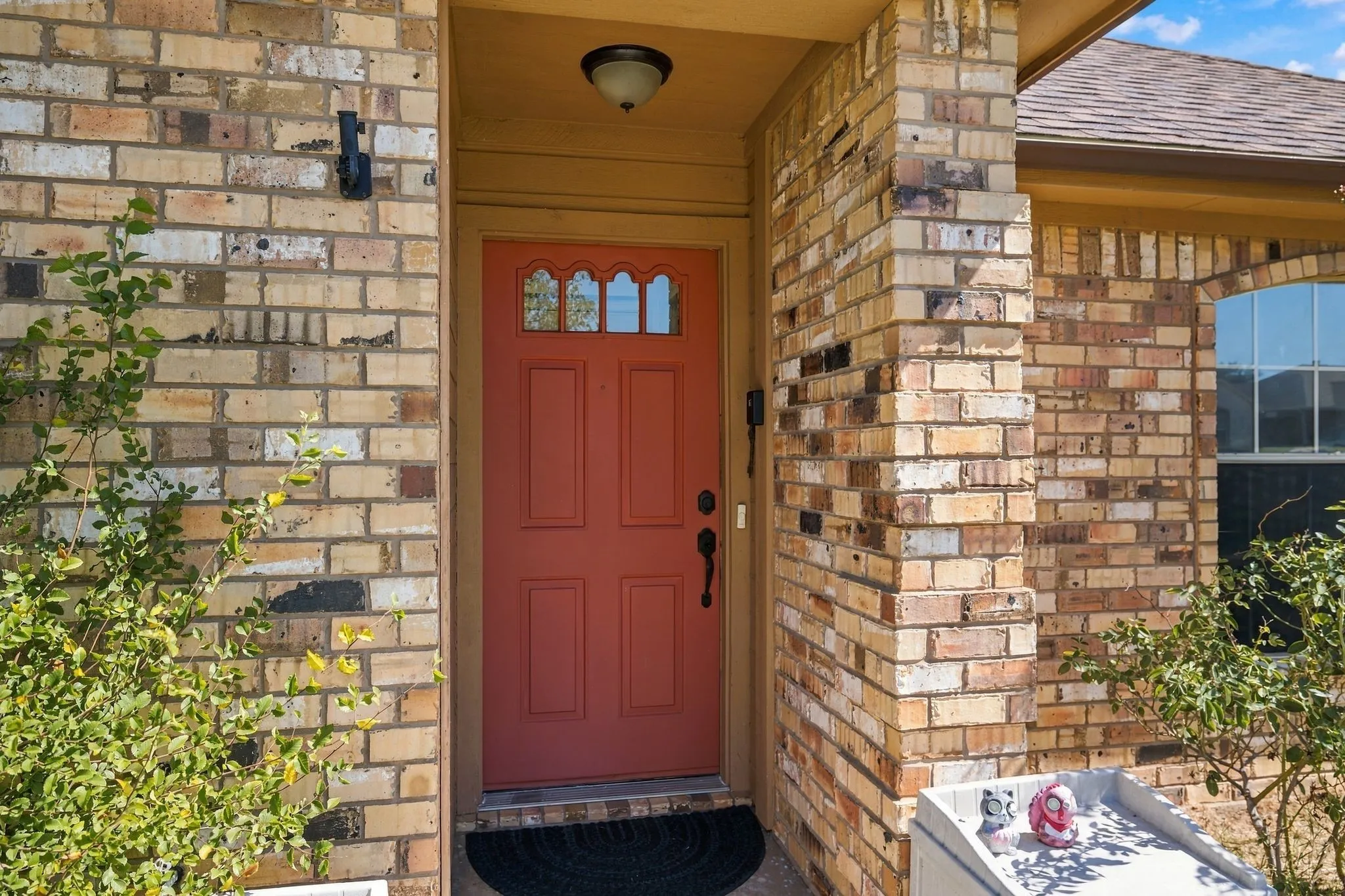 Brick exterior with a vibrant red entry door featuring decorative glass lites, a shingled roof, and an arched window